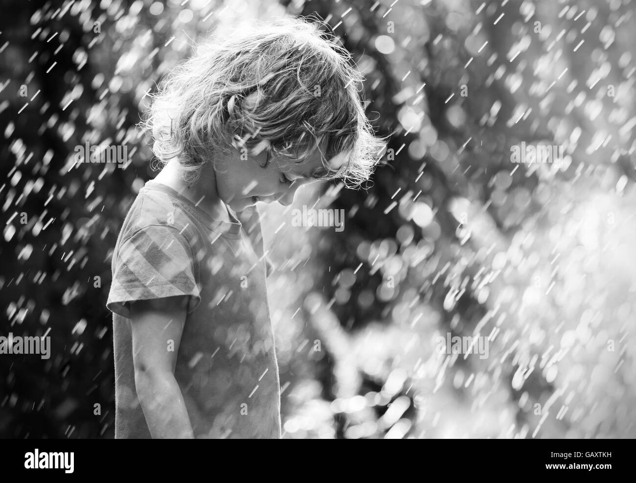 Photo of happy little girl standing under summer rain. Black and white Stock Photo