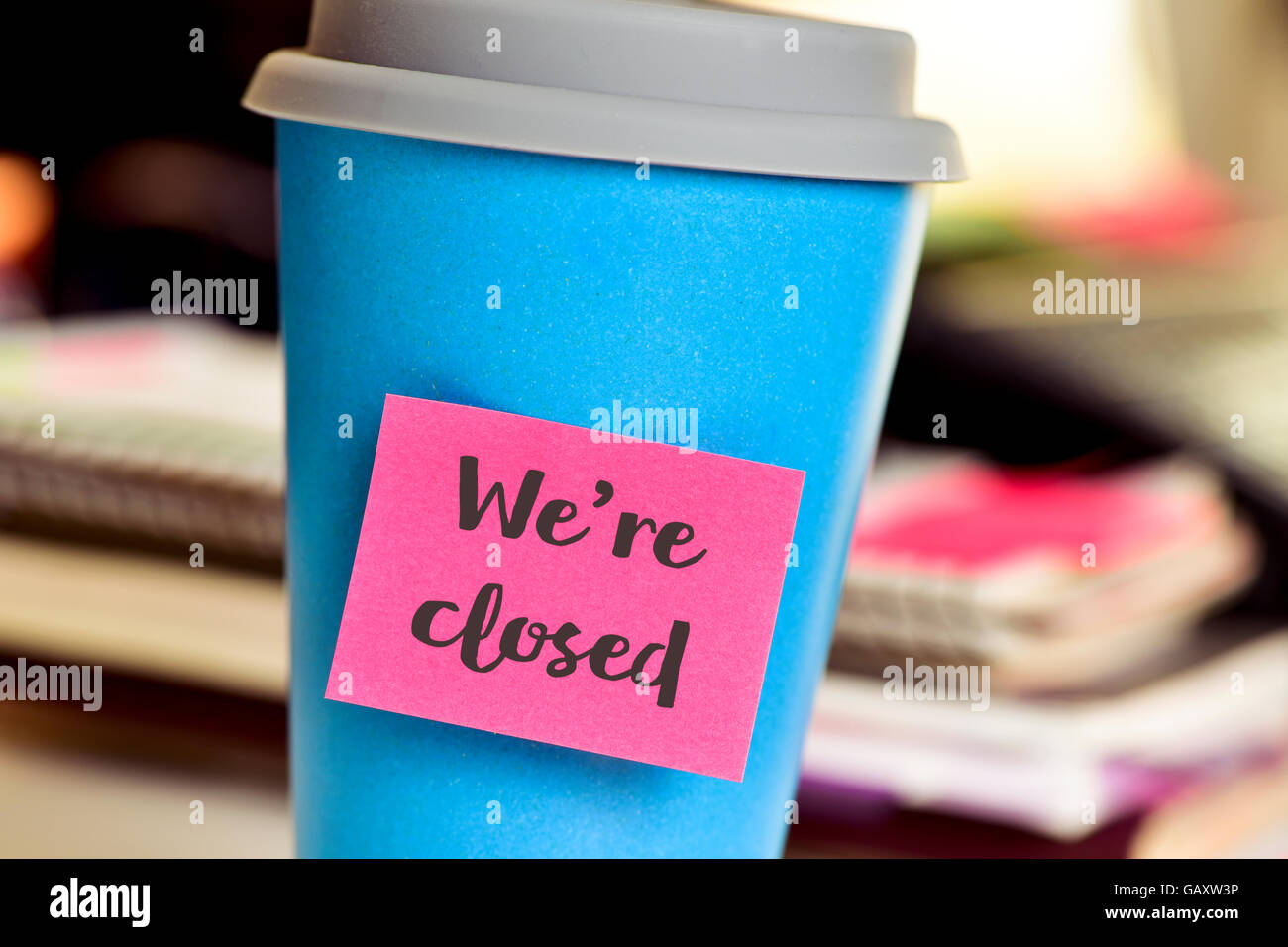 closeup of a blue mug with a pink sticky note with the text we are closed, on an office desk Stock Photo
