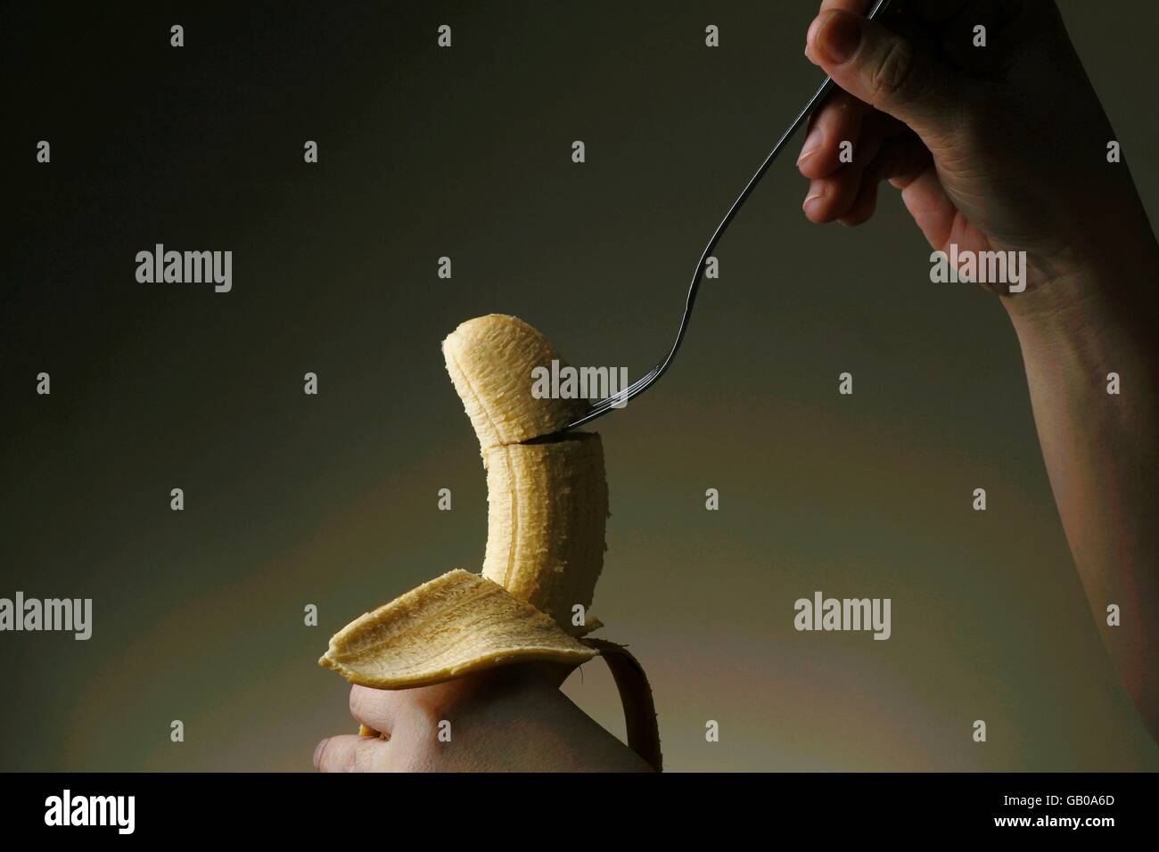 Hand sticking a fork on a ripe banana Stock Photo