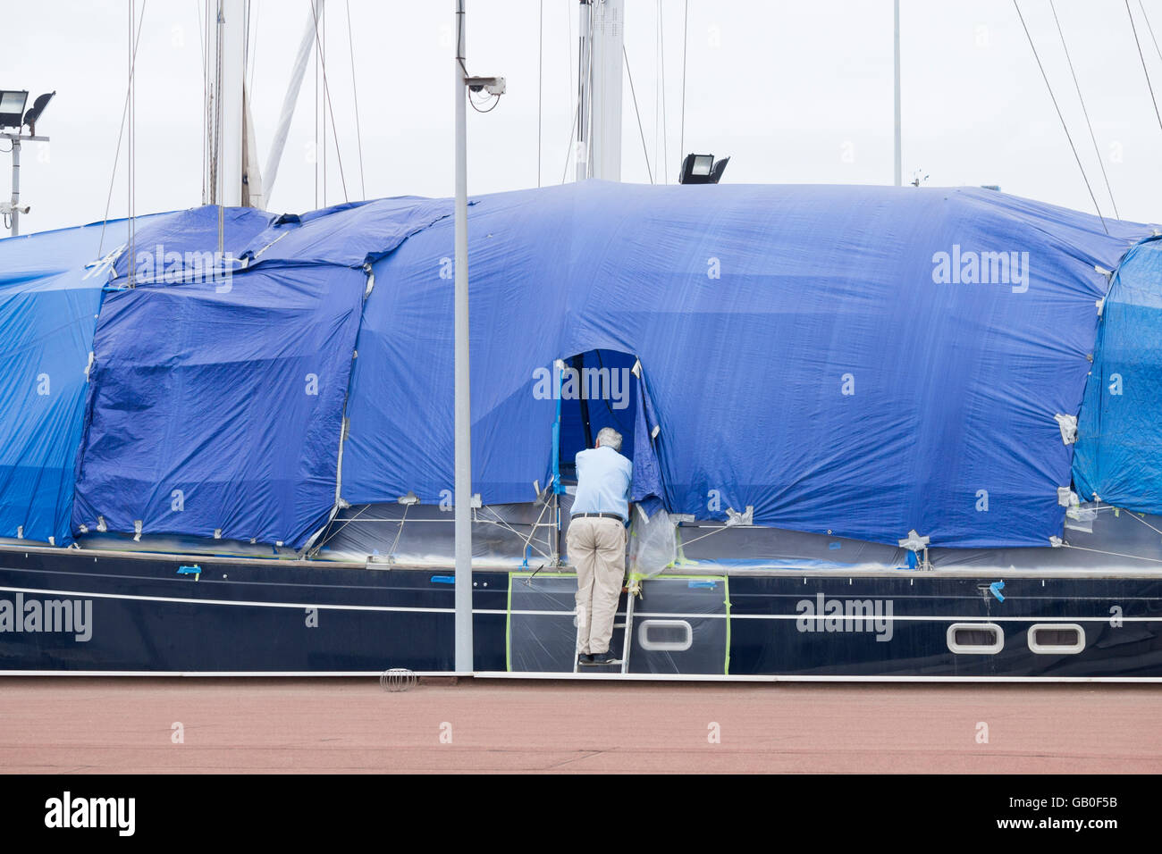 Elderly man repairing yacht while dog watches him from deck in boatyard in Las Palmas on Gran Canaria, Canary Islands, Spain Stock Photo