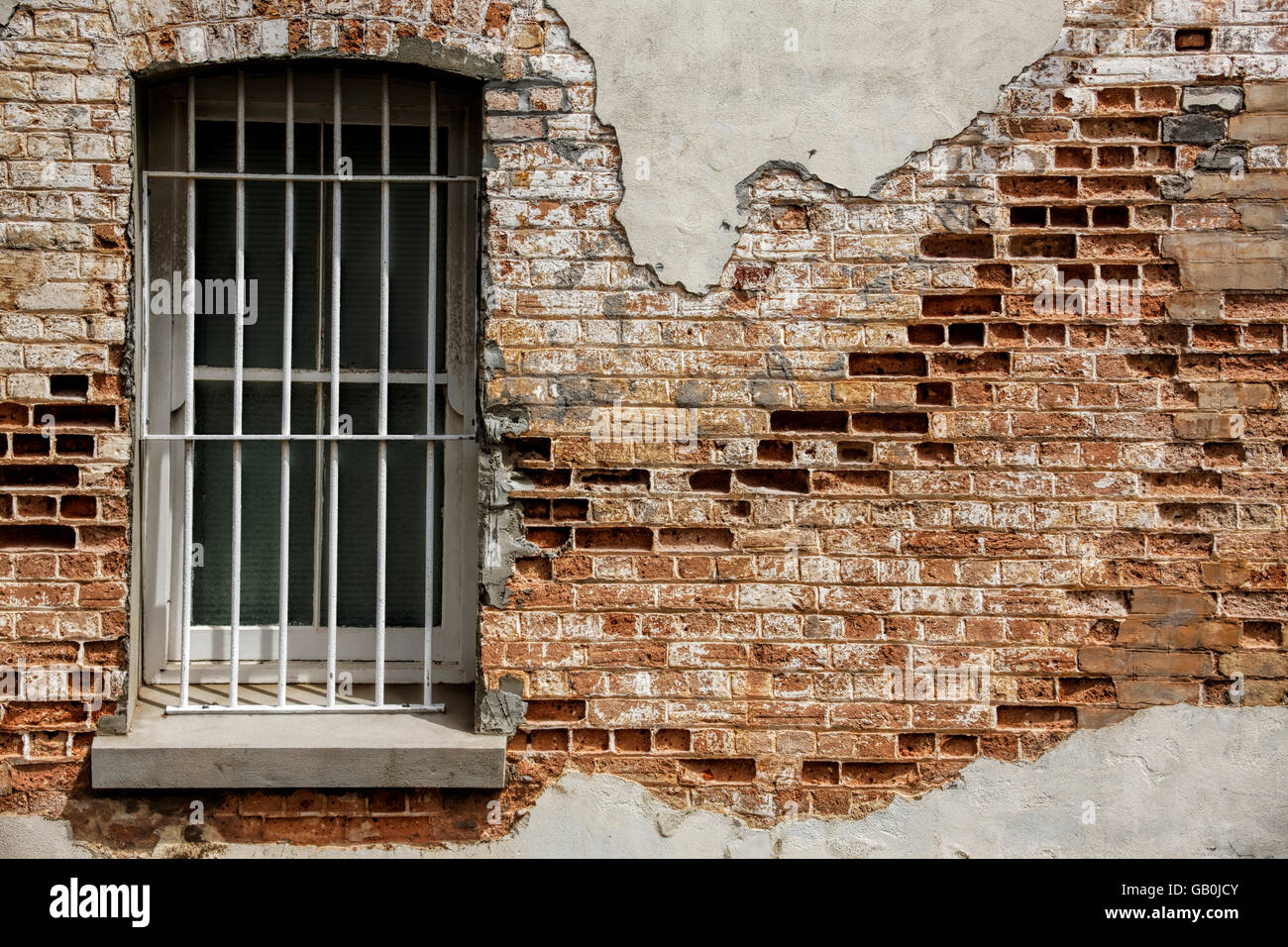 Old window with bars set into decaying clay brick wall, Albany Western Australia Stock Photo