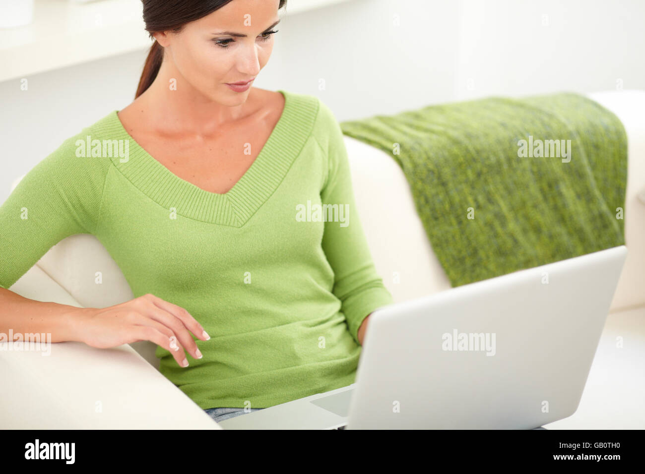 Caucasian young female in a green shirt using a laptop while sitting ...