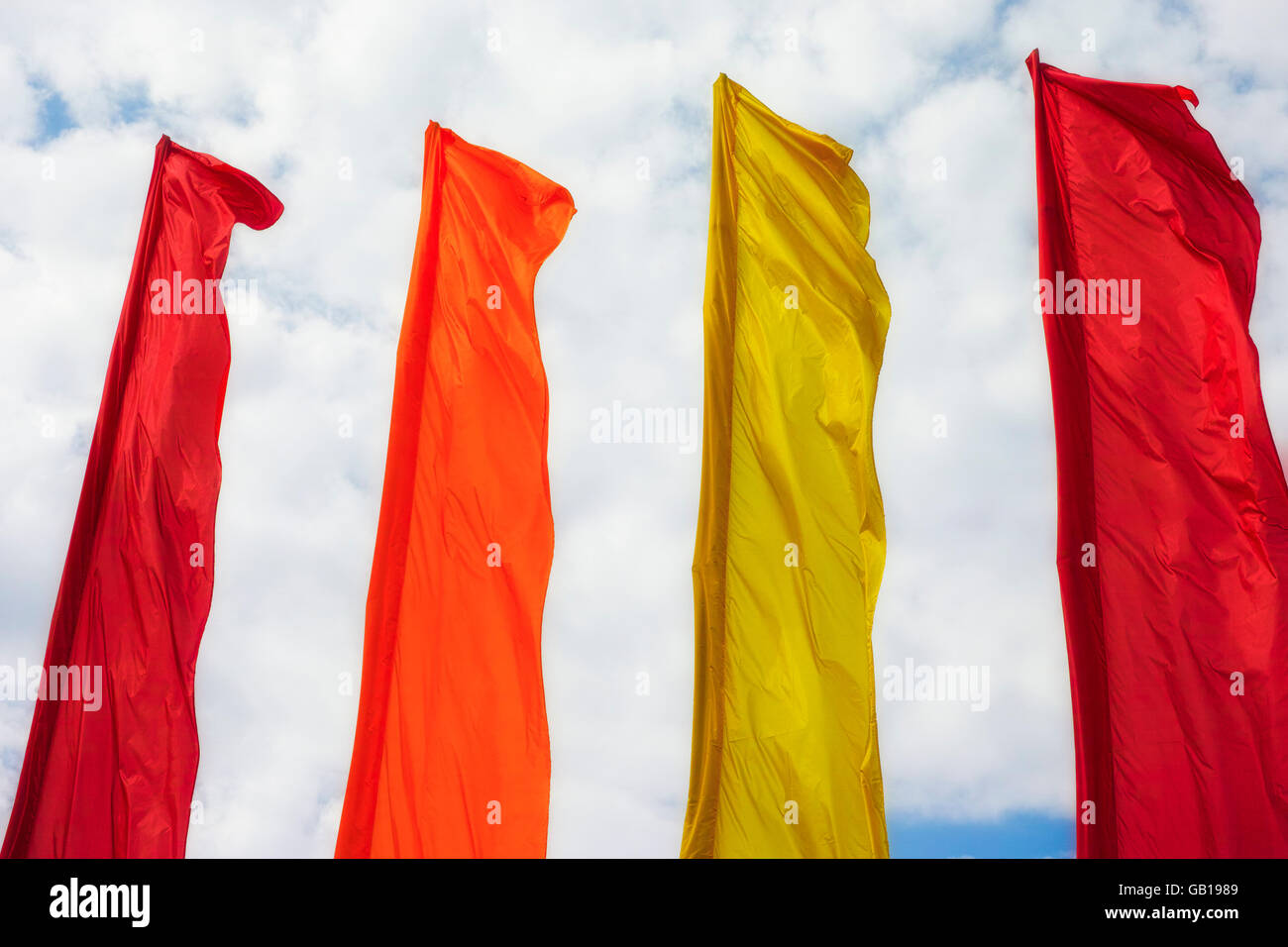 Row of big colorful flags blowing in wind against cloudy sky background ...