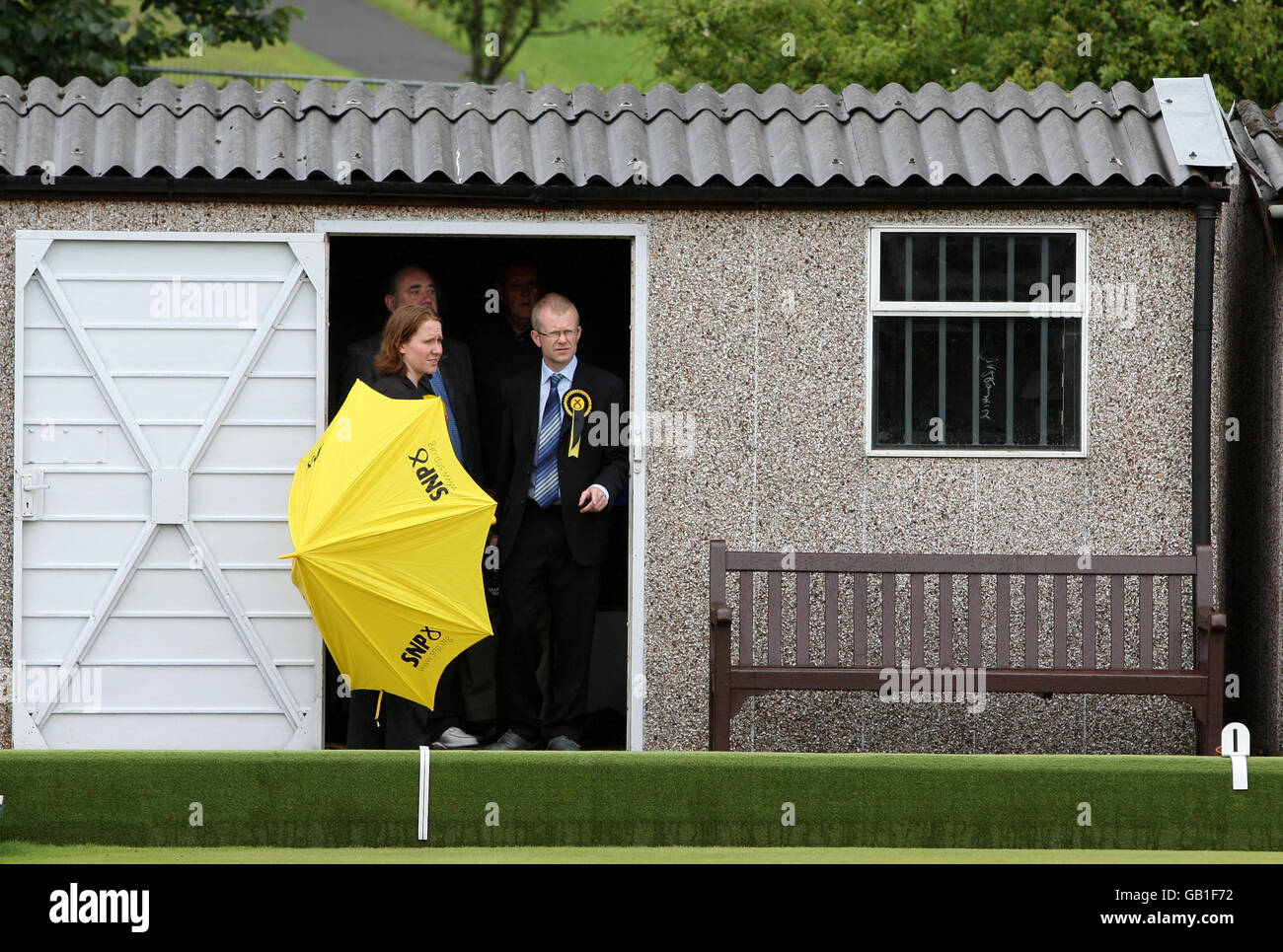 SNP candidate for Glasgow East, John Mason (right) with First Minister Alex Salmond (partly obscured) taking shelter while visiting Garrowhill Bowling Club, to highlight support for pensioners in the citys east end. Stock Photo