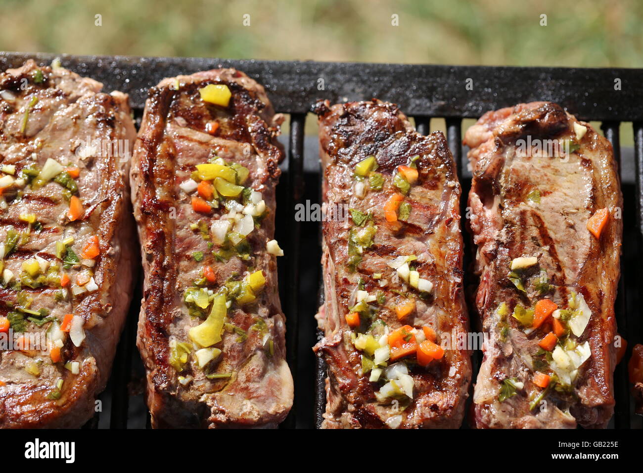Beef Meat with Chimichurri Sauce. Pieces of Beef Meat with Chimichurri Sauce on the Grill, Close Up. Raw sinta meat, raw flesh. Red meat Stock Photo
