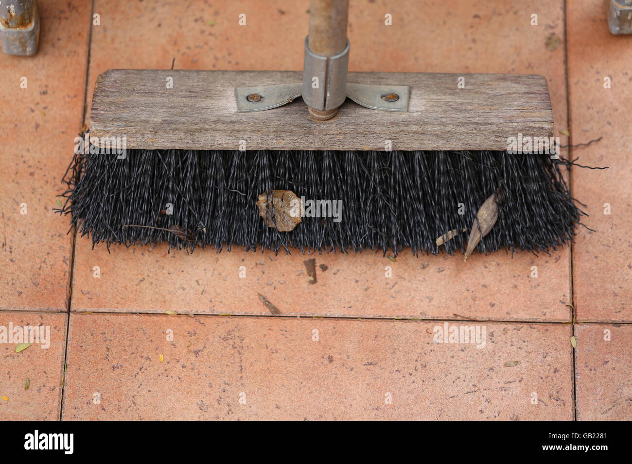 Broom. Wooden outdoor broom with synthetic hair on brown terracotta floor tile. Ladder legs in the photo corners. Stock Photo