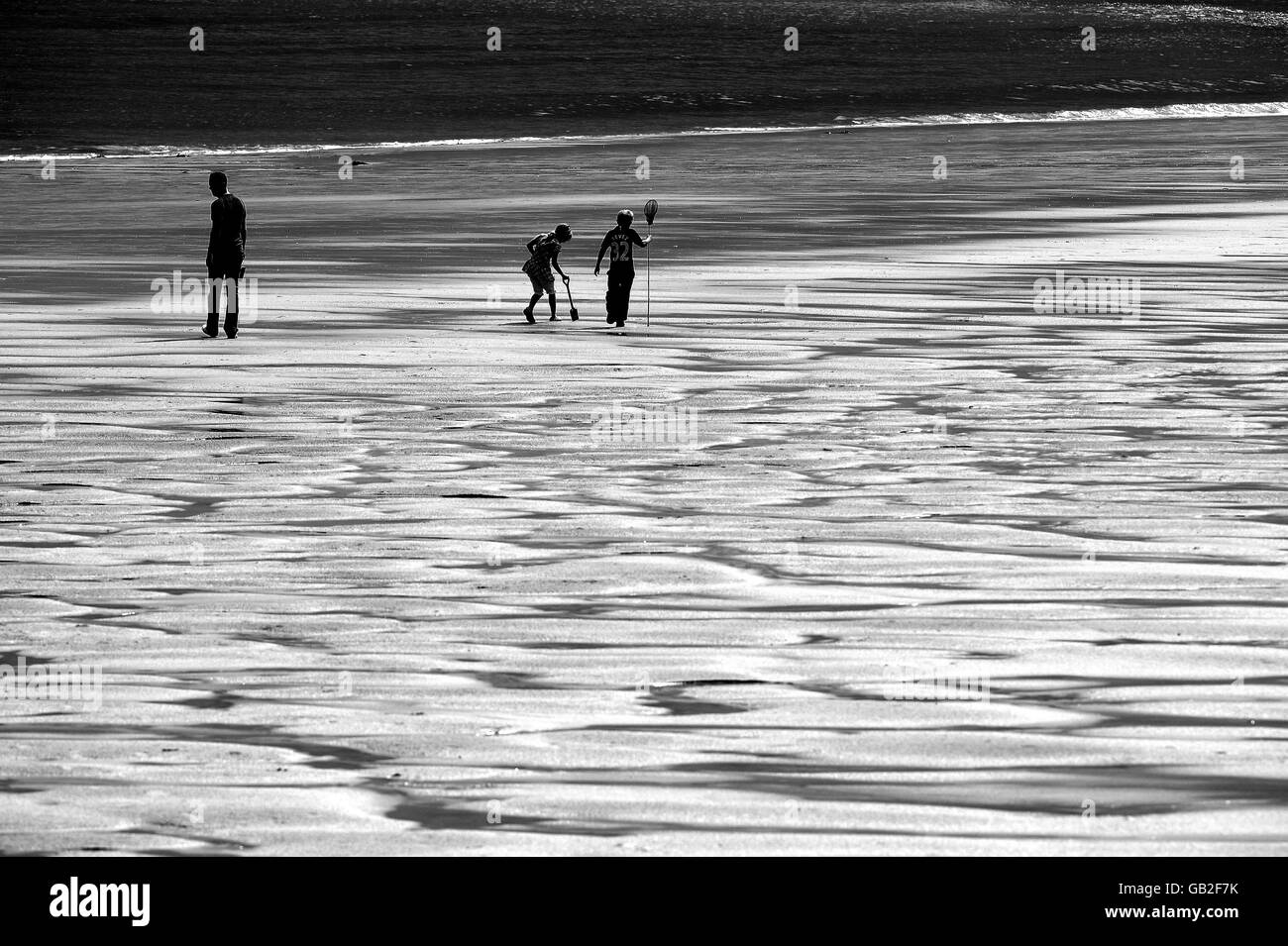 PHOTO TAKEN IN BLACK AND WHITE Three people walk on Whitley Bay beach after a storm passed over the North East coast. Stock Photo