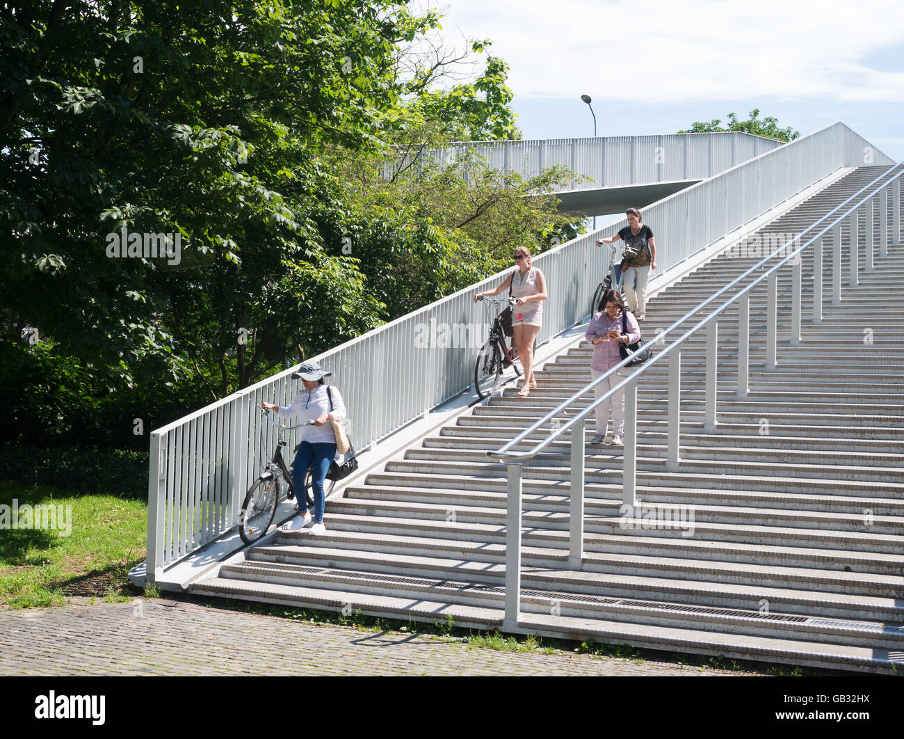 Three young women wheeling bicycles down a runnel or gutter on steps from bridge, Maastricht, Holland, Europe Stock Photo