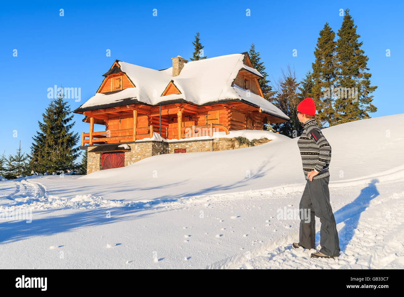 Young woman tourist standing in fresh snow in front of a mountain hut in Gorce Mountains in winter season, Poland Stock Photo