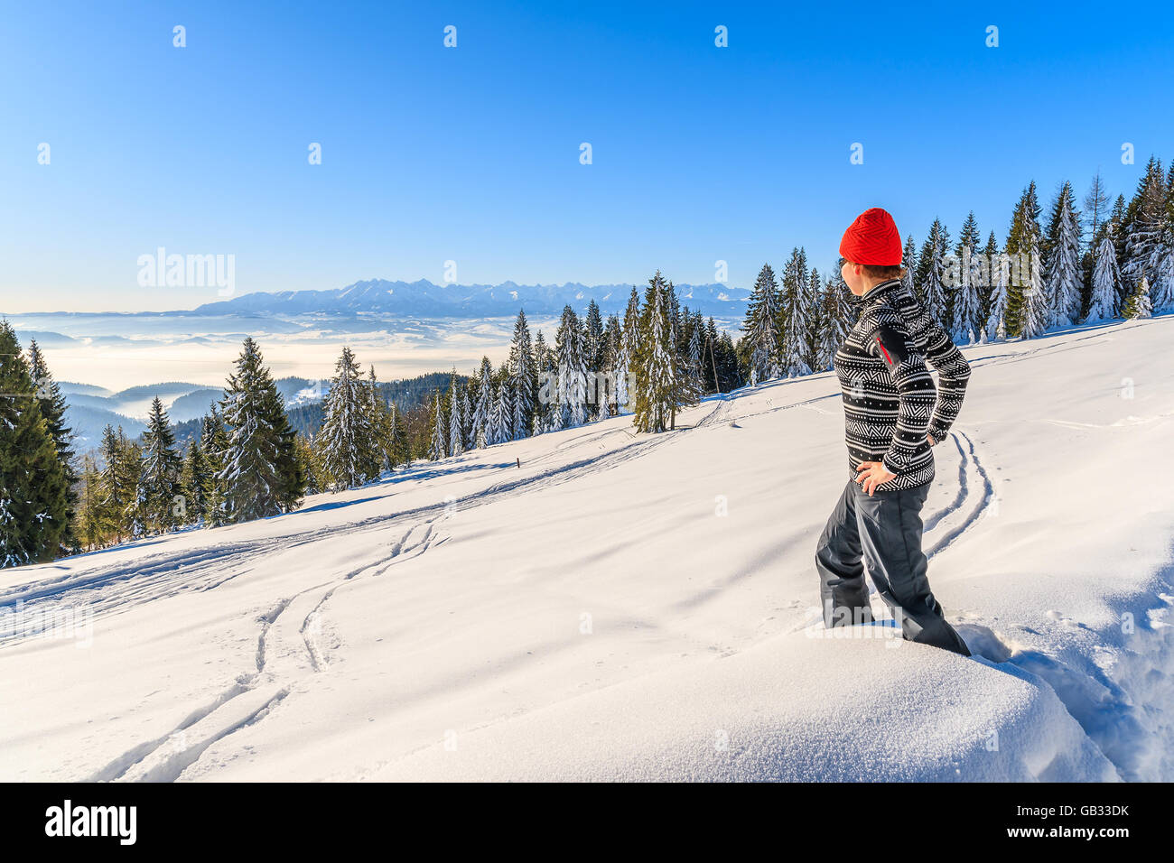 Young woman tourist standing in deep snow in Gorce Mountains looking at distant Tatry Mountains panorama, Poland Stock Photo