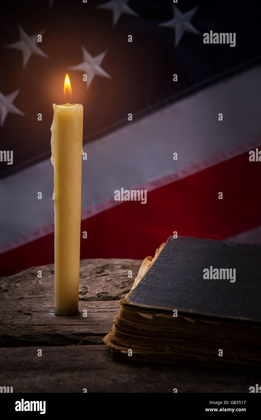 Burning candle and old book. Flag of USA by candlelight. Wooden table