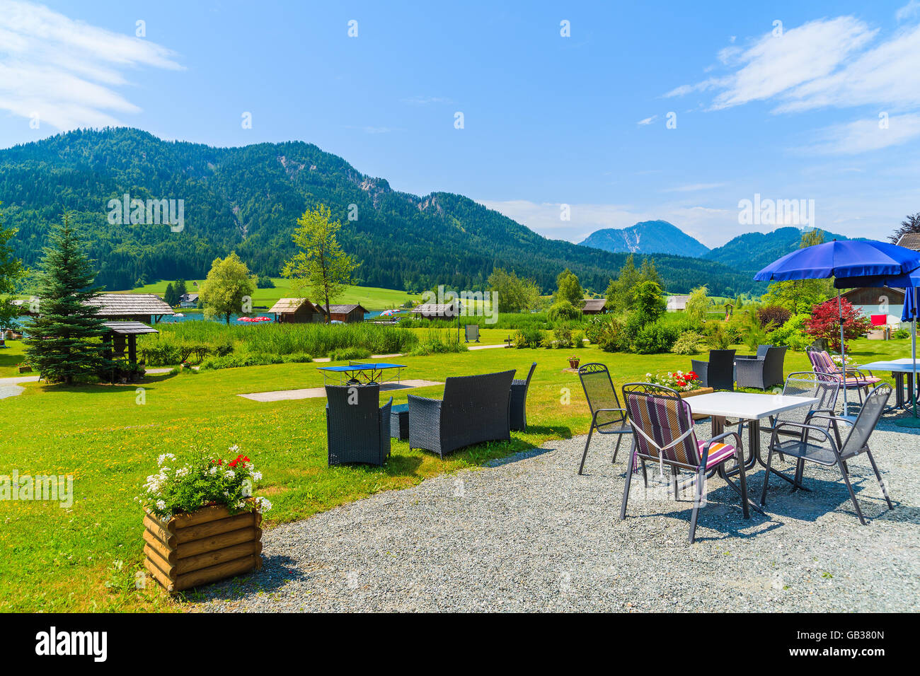 Tables in garden of a guest house on shore of Weissensee lake in summer landscape of Alps Mountains, Austria Stock Photo
