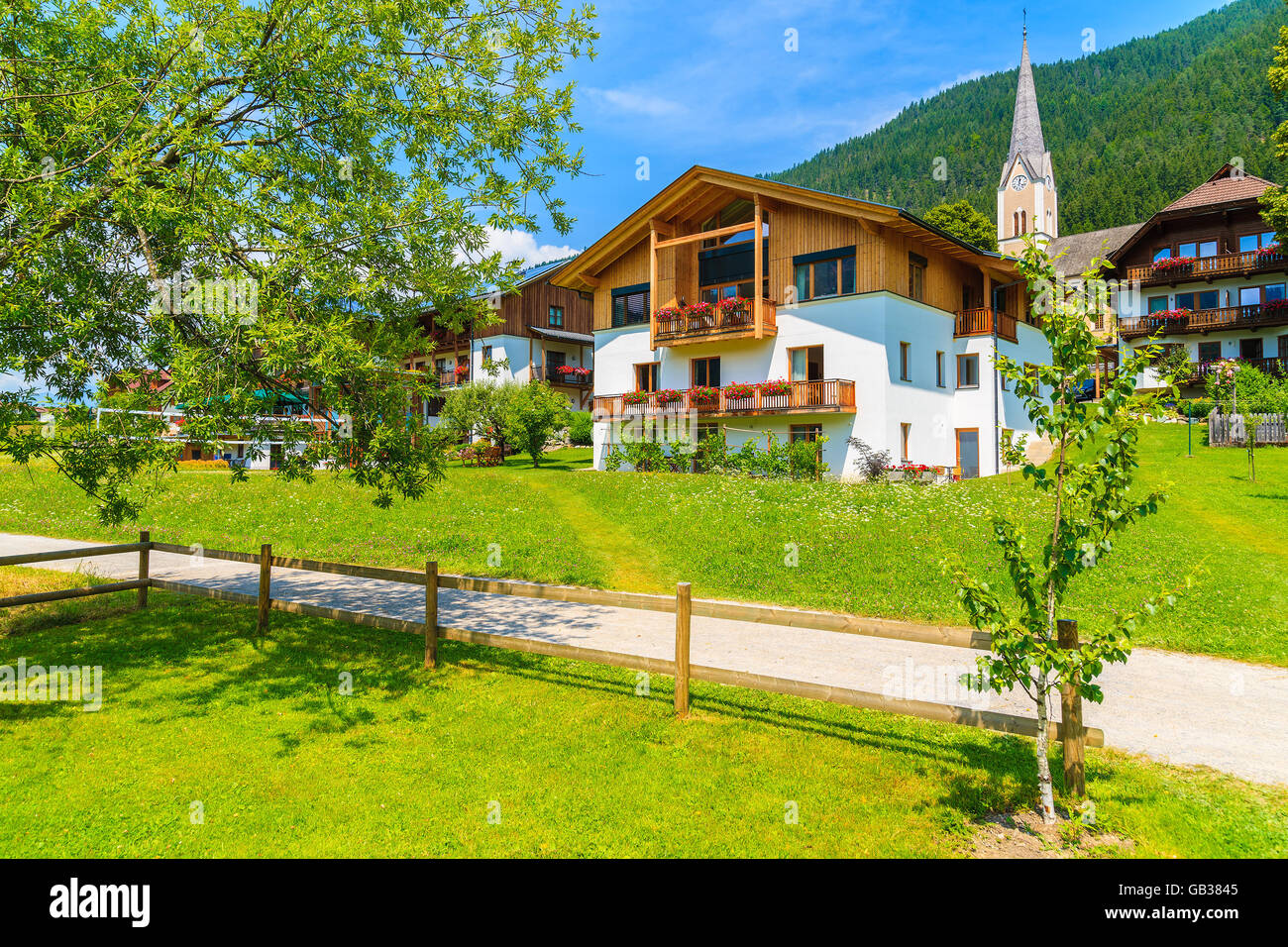Walking path along alpine village with traditional countryside houses on shore of Weissensee lake in summer landscape of Alps Mo Stock Photo