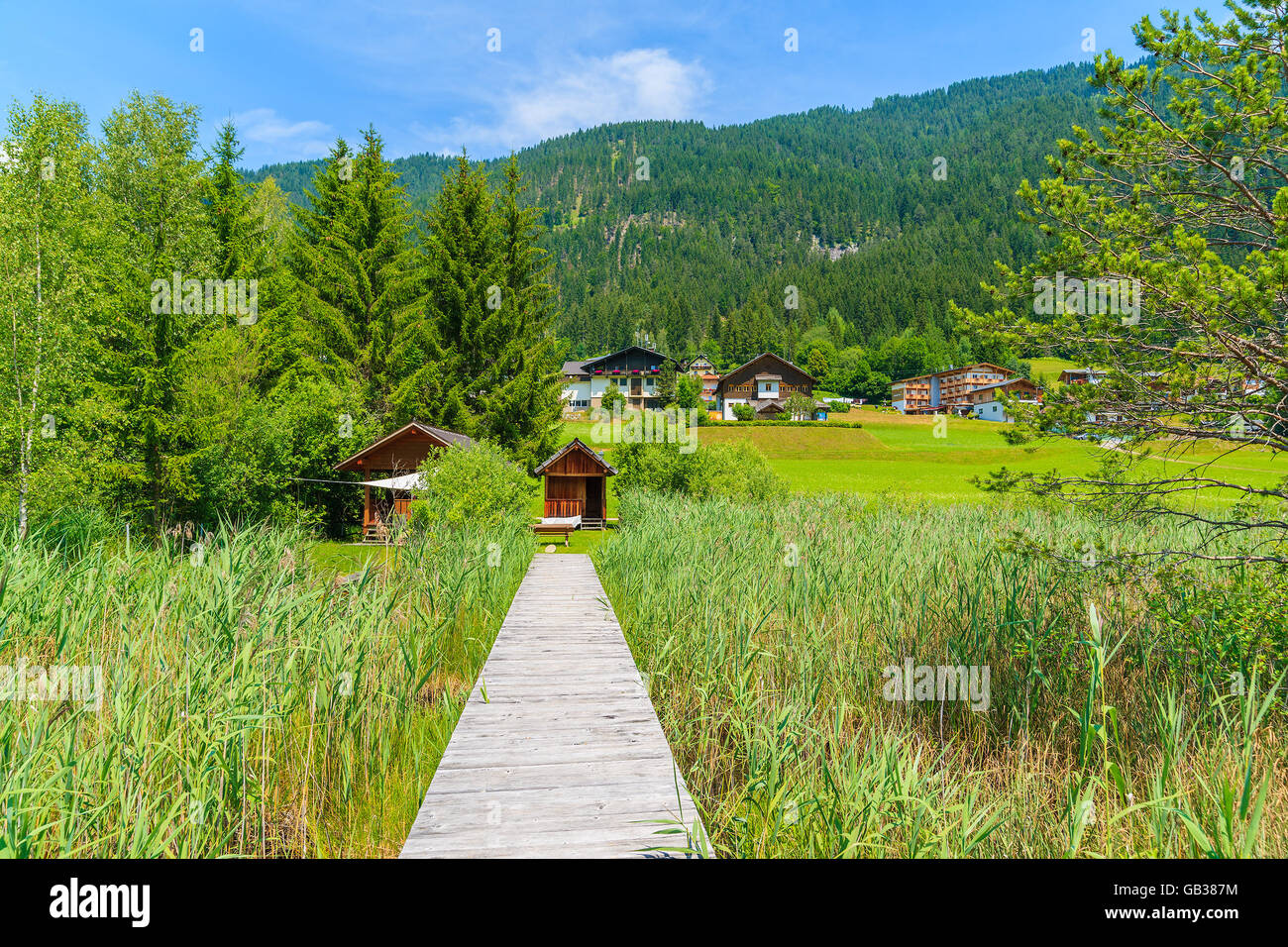 Wooden jetty in grass in alpine village on shore of Weissensee lake in summer landscape of Alps Mountains, Austria Stock Photo