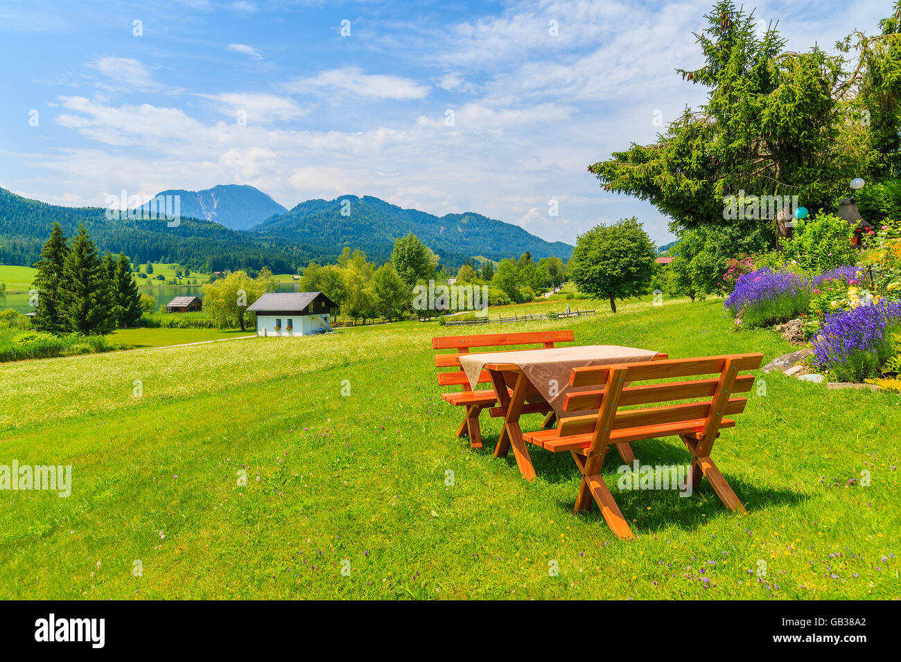 Benches with picnic table on green grass in alpine village on shore of Weissensee lake in summer landscape of Alps Mountains, Au Stock Photo