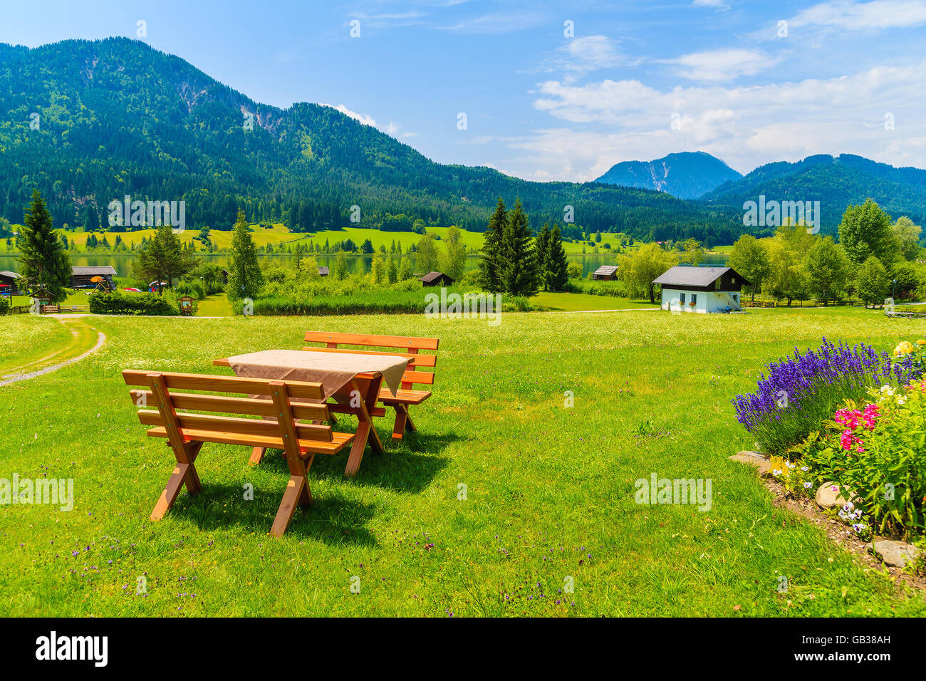 Benches with picnic table on green grass in alpine village on shore of Weissensee lake in summer landscape of Alps Mountains, Au Stock Photo
