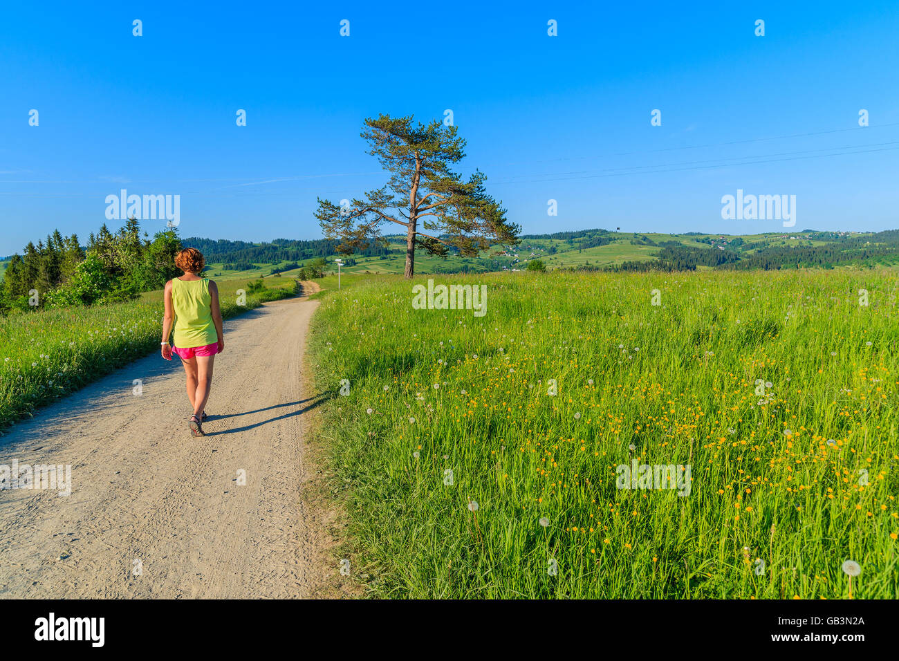 Young woman tourist walking on rural road along green meadow in Tatra Mountains, Poland Stock Photo