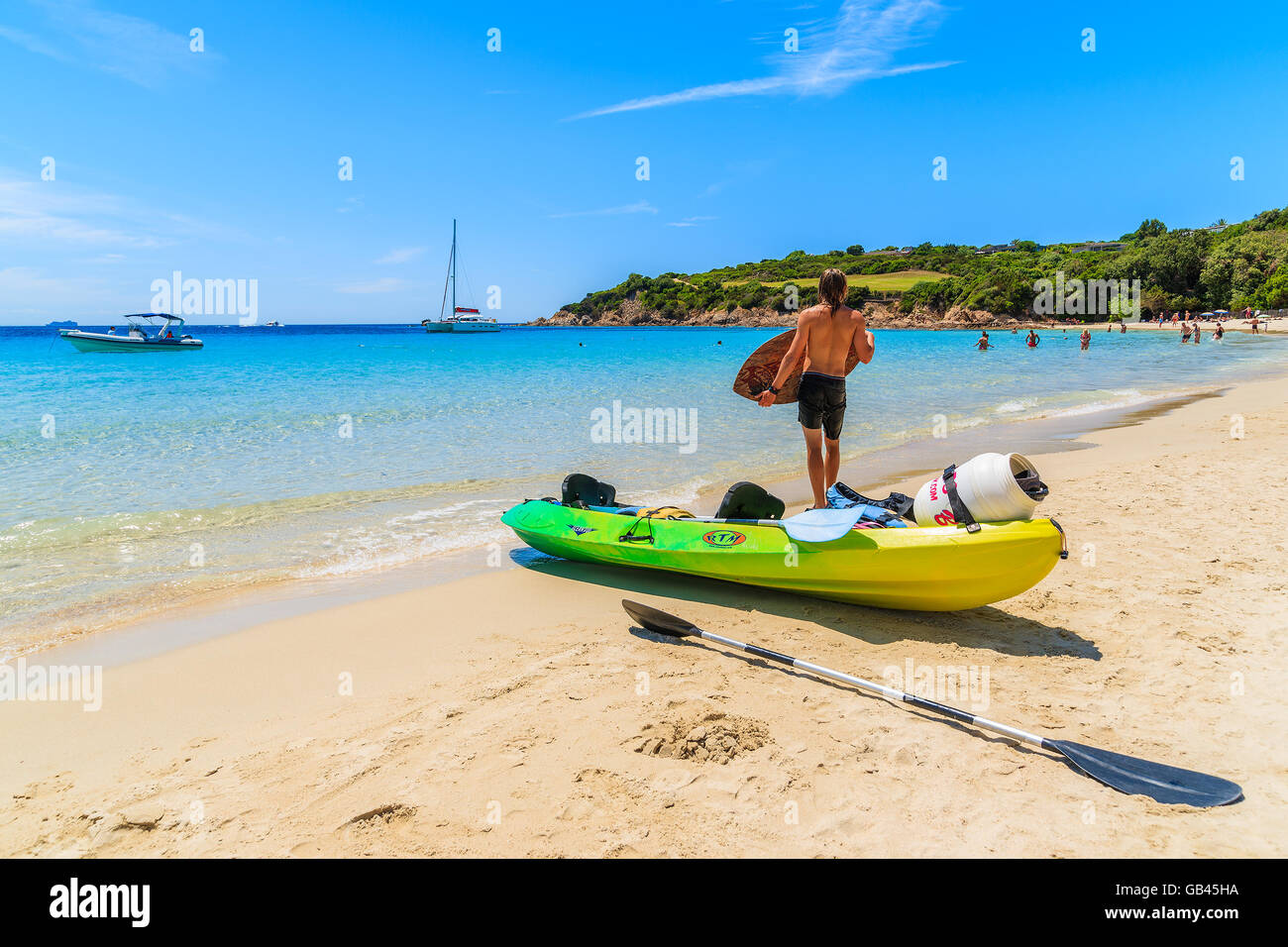 CORSICA ISLAND, FRANCE - JUN 25, 2015: young man standing by kayak and preparing for surfing on sandy Grande Sperone beach, Cors Stock Photo
