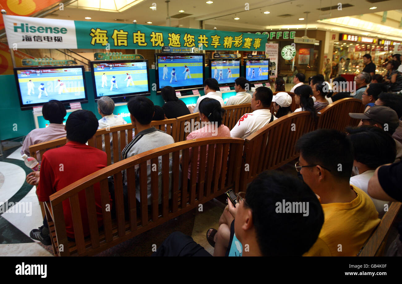 Shoppers stop to watch Olympic coverage in the Jusco shopping centre, Qingdao. China. Stock Photo