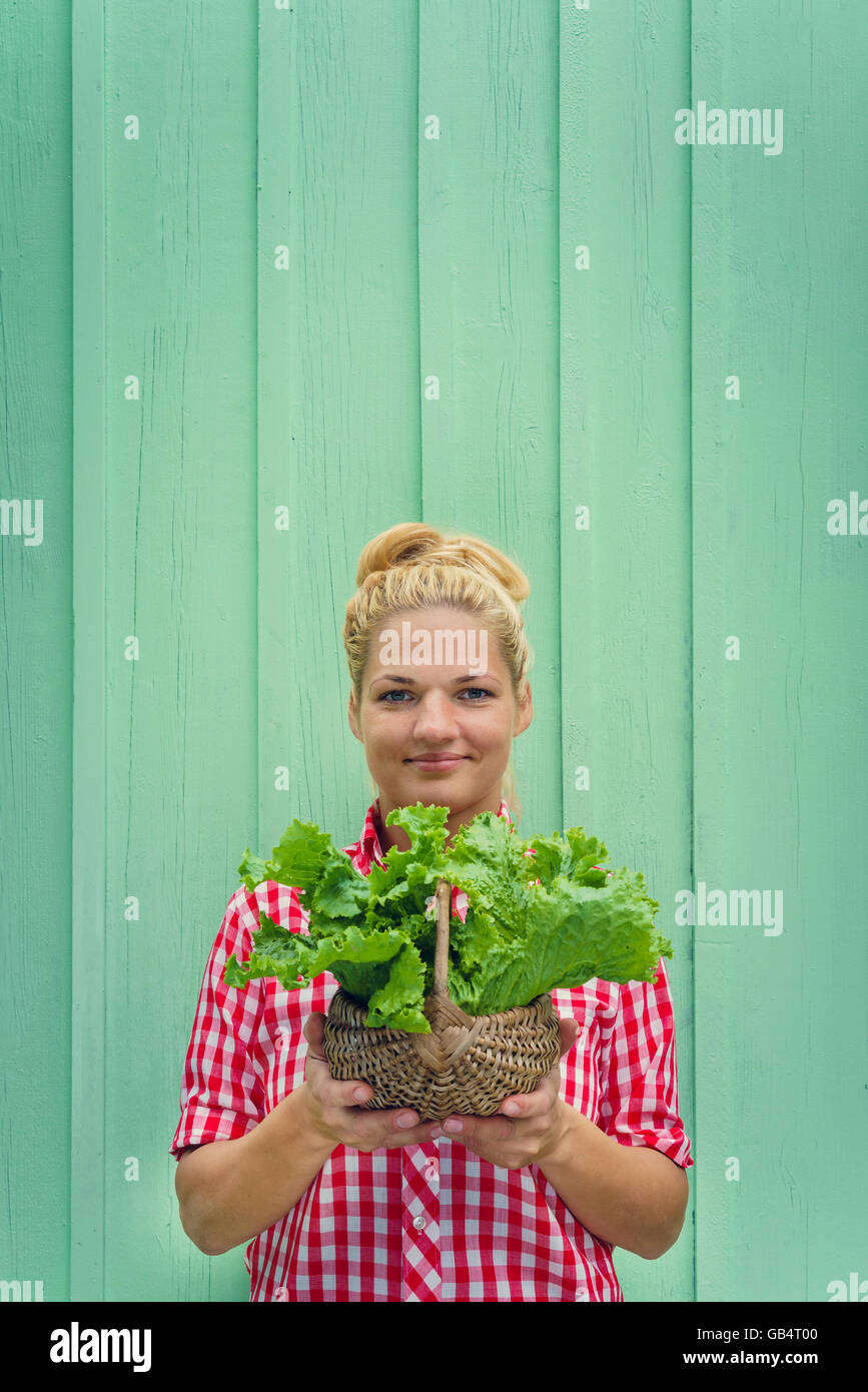Blonde girl on a turquoise background holding basket with lettuce ...