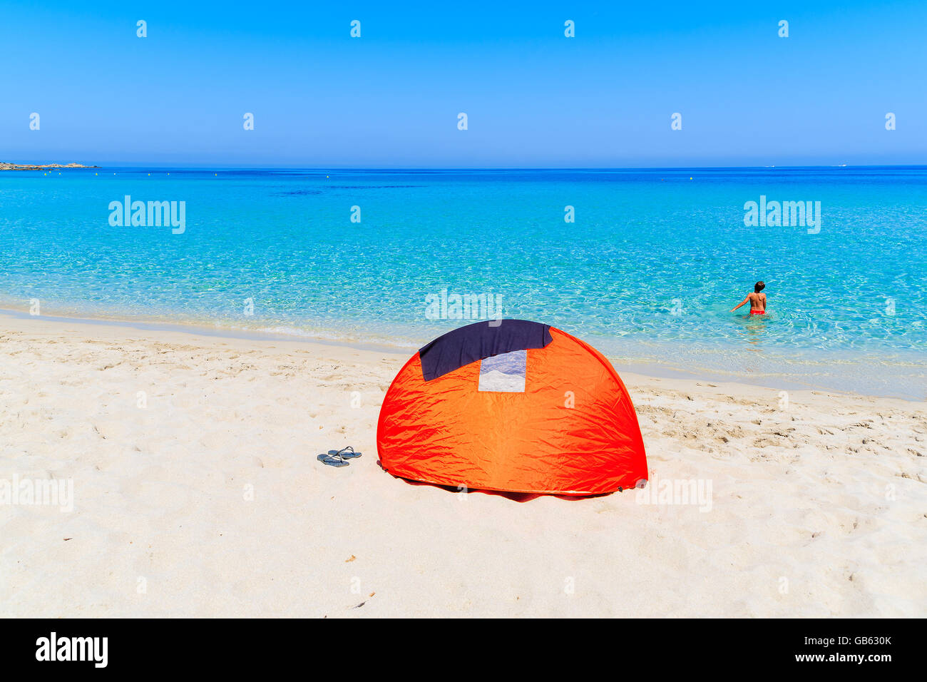 Sunshade tent on sandy Bodri beach and young boy relaxing in water, Corsica island, France Stock Photo