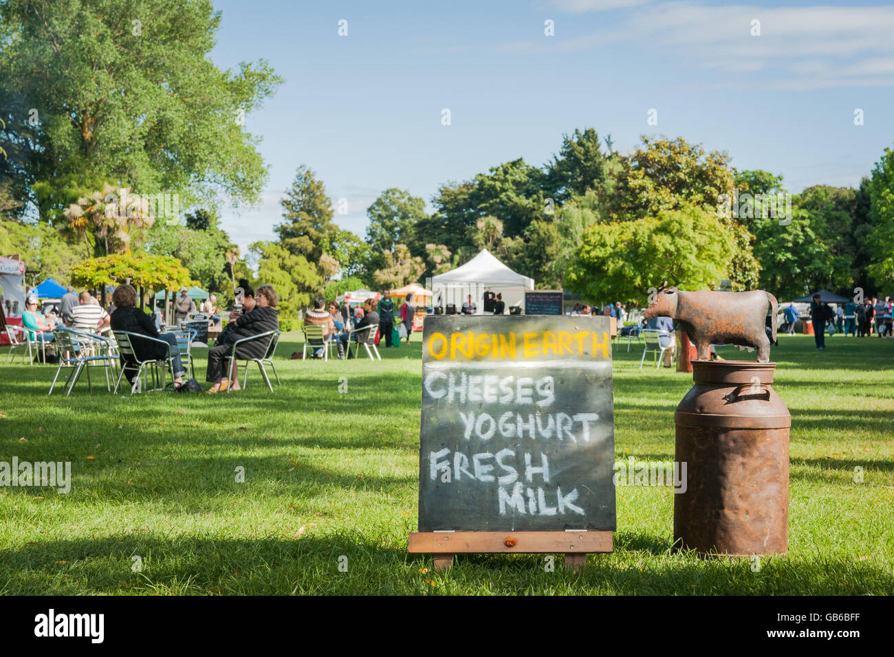 Weekend Farmers Market sign with groups of people sitting around tables relaxing in shade Stock Photo