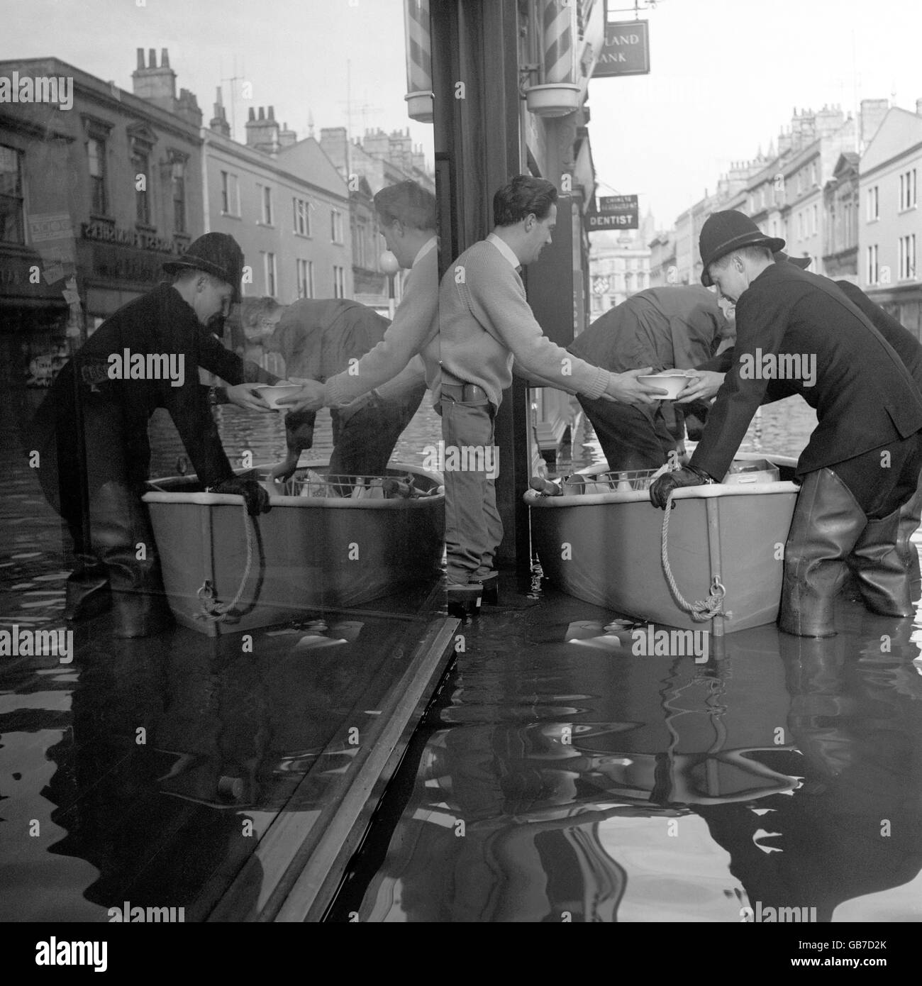Reflected in a shop window, wader-clad police unload food provisions from a small boat to a resident in Southgate Street, Bath, Somerset. Stock Photo