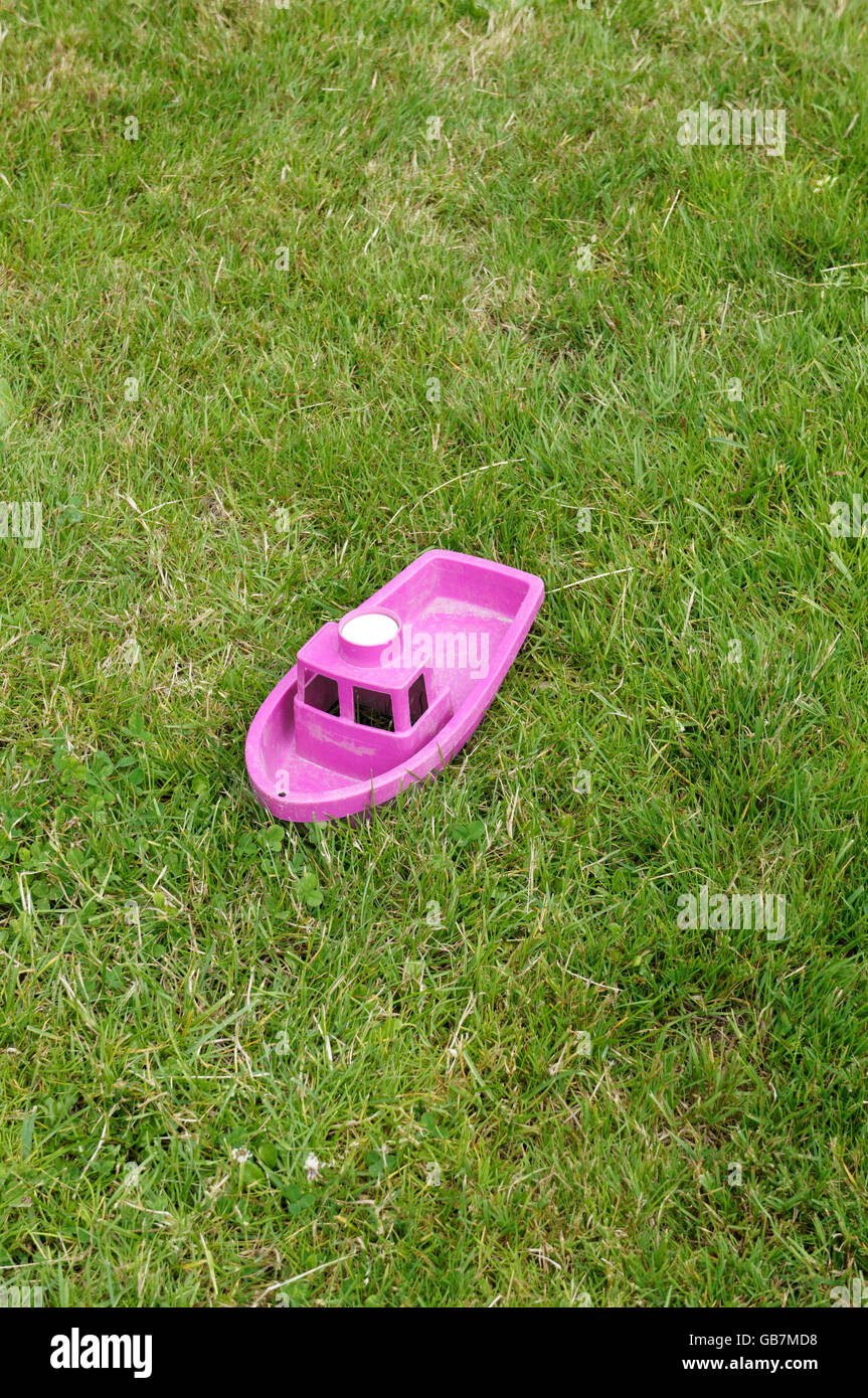A child s toy plastic hot pink plastic boat sitting alone in green grass Stock Photo Alamy