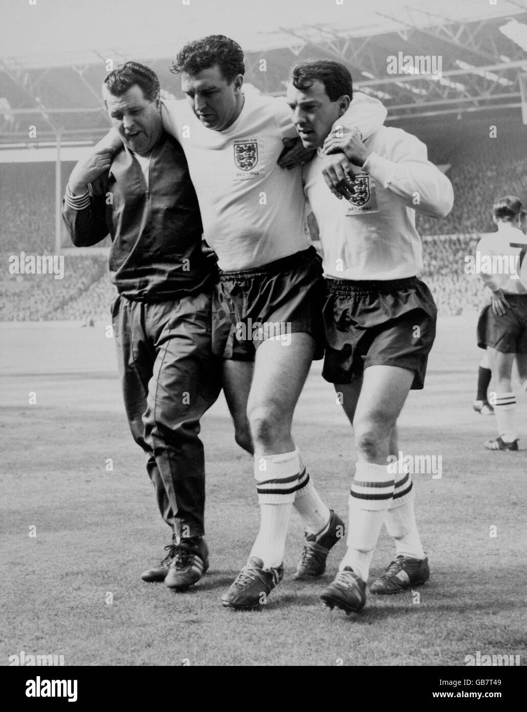 England's Bobby Smith (c) is helped off the pitch by teammate Jimmy Greaves (r) and trainer Harold Shepherdson (l) after badly bruising his knee in a collision with Scotland's Eric Caldow, who suffered a broken leg Stock Photo