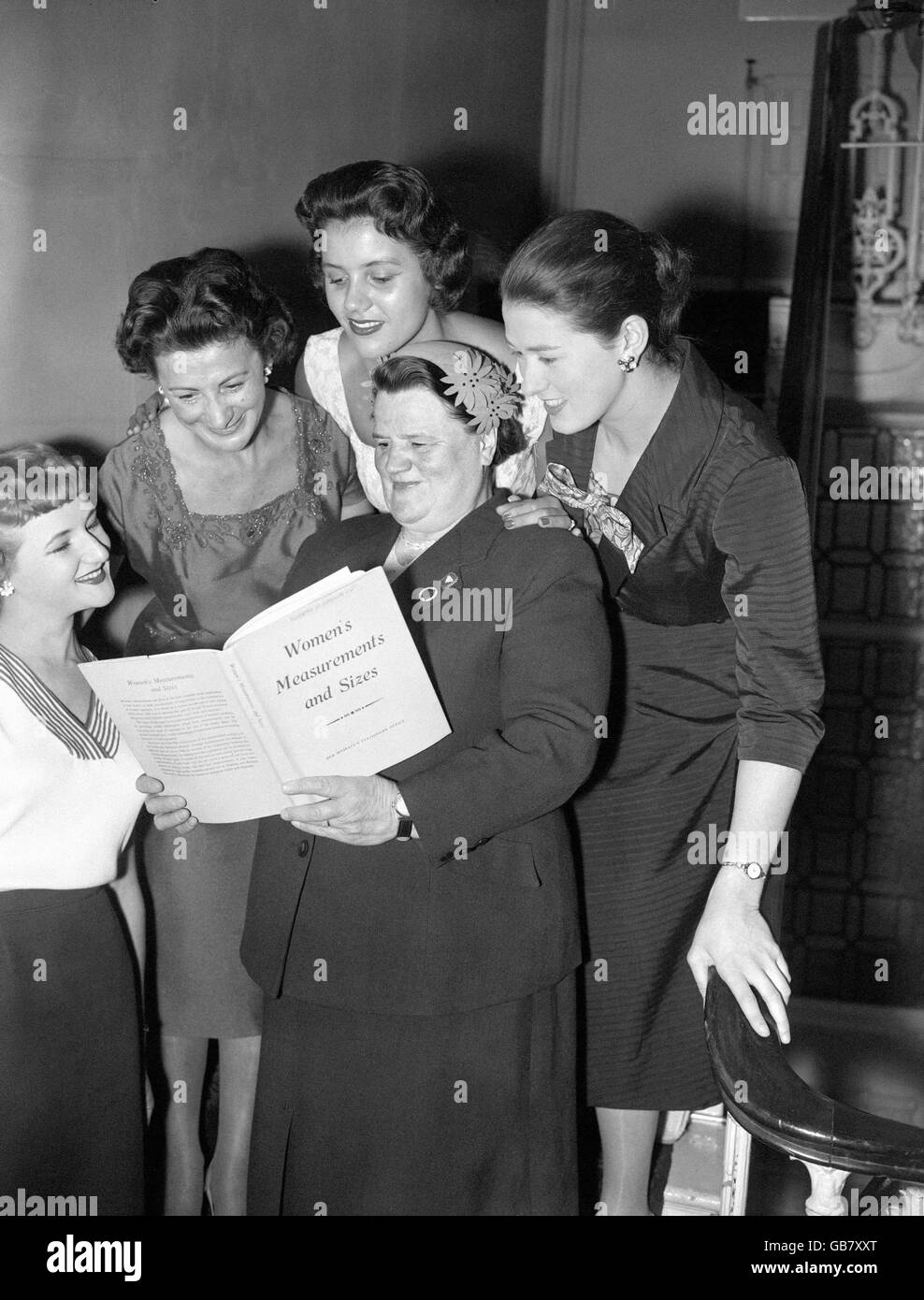 M.P. Bessie Braddock reads the report on woman's measurements and sizes. Looking over her shoulder from left to right are Miss Small, Miss Regular, Miss Medium, and Miss Tall. These are figures standardised in the report, the most comprehensive 'vital statistics' study undertaken in the Britain. Bessie Braddock took the chair in the press conference in connection with the report. The inquiry sought to provide up to date scientific data of Britain's women to aid manufacturers of womens clothes. Stock Photo
