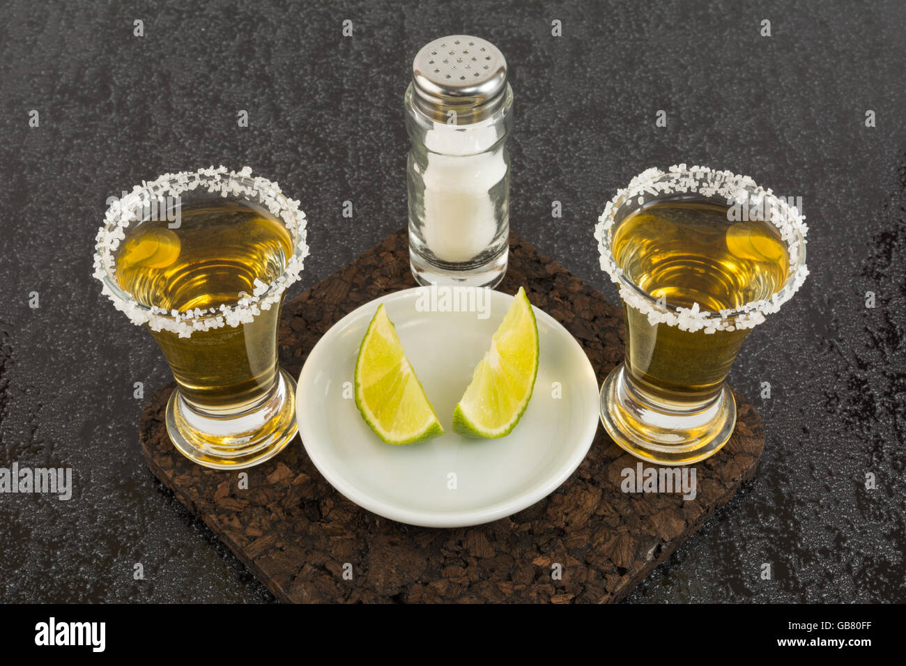 Two shots of gold tequila with lime and salt on the black background