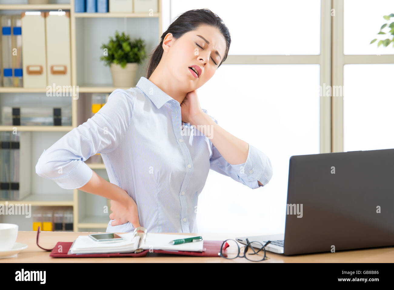 Young asian business woman with pain in neck in office Stock Photo