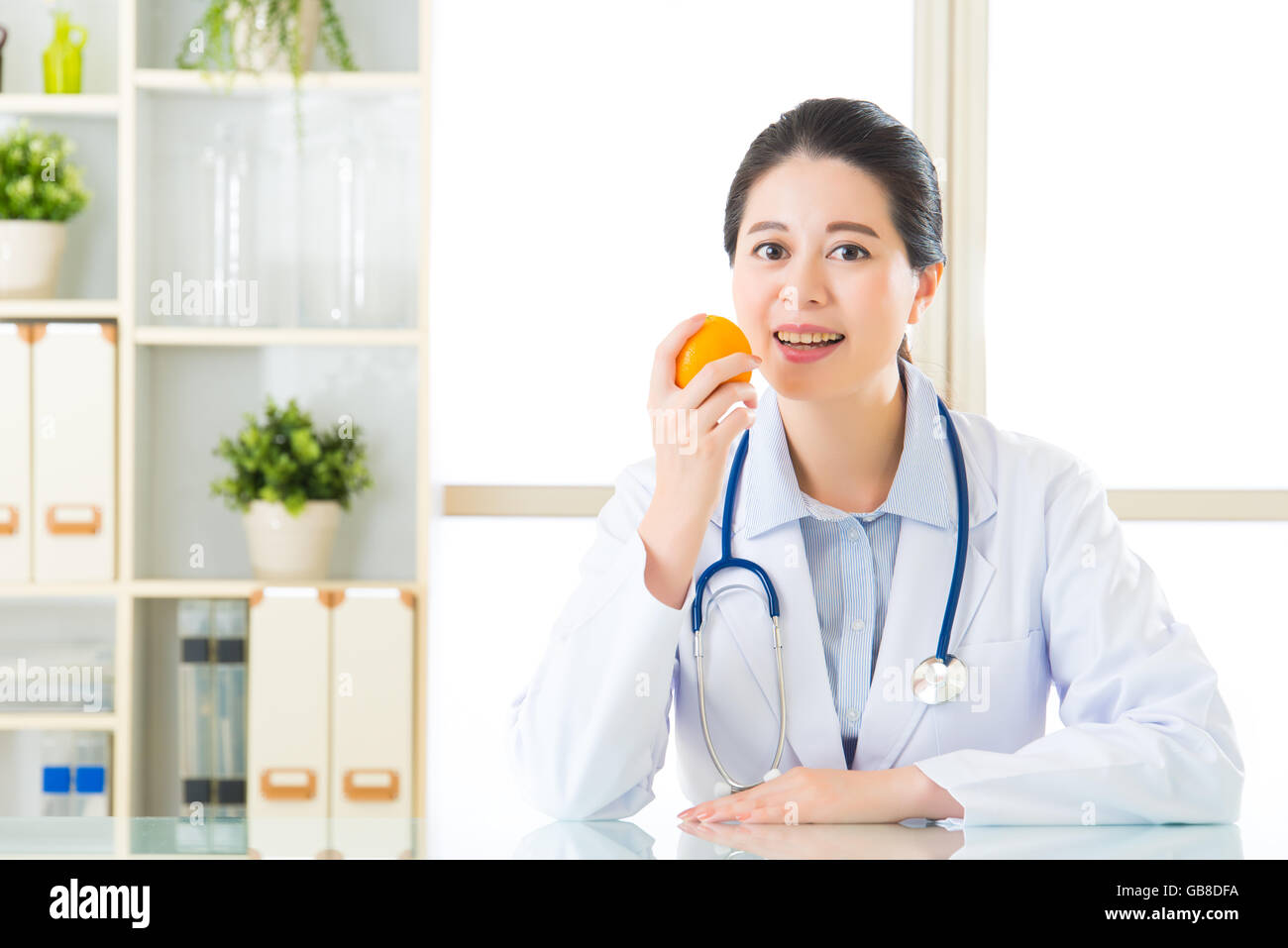 Young asian nutritionist eating an orange, healthy eating Stock Photo