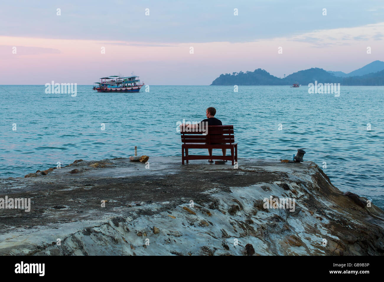 Lone man sitting on a bench at the evening sea coast Stock Photo - Alamy