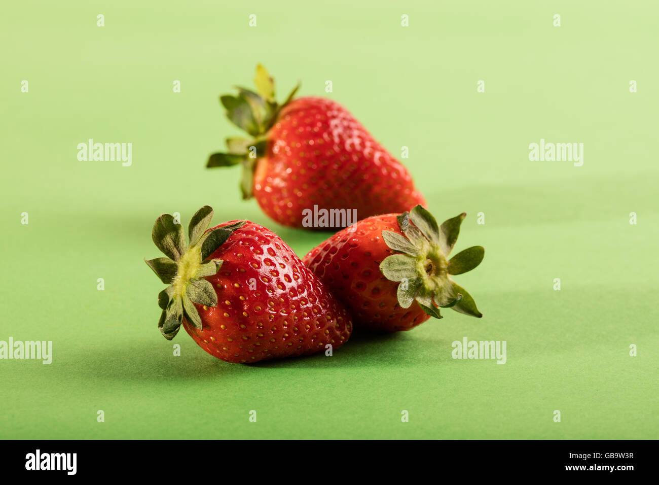 Three juicy strawberry on green background Stock Photo - Alamy
