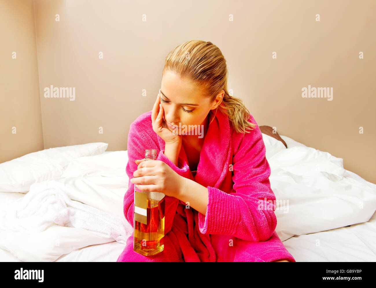 Young woman sitting on the bed crying and drinking whiskey Stock Photo