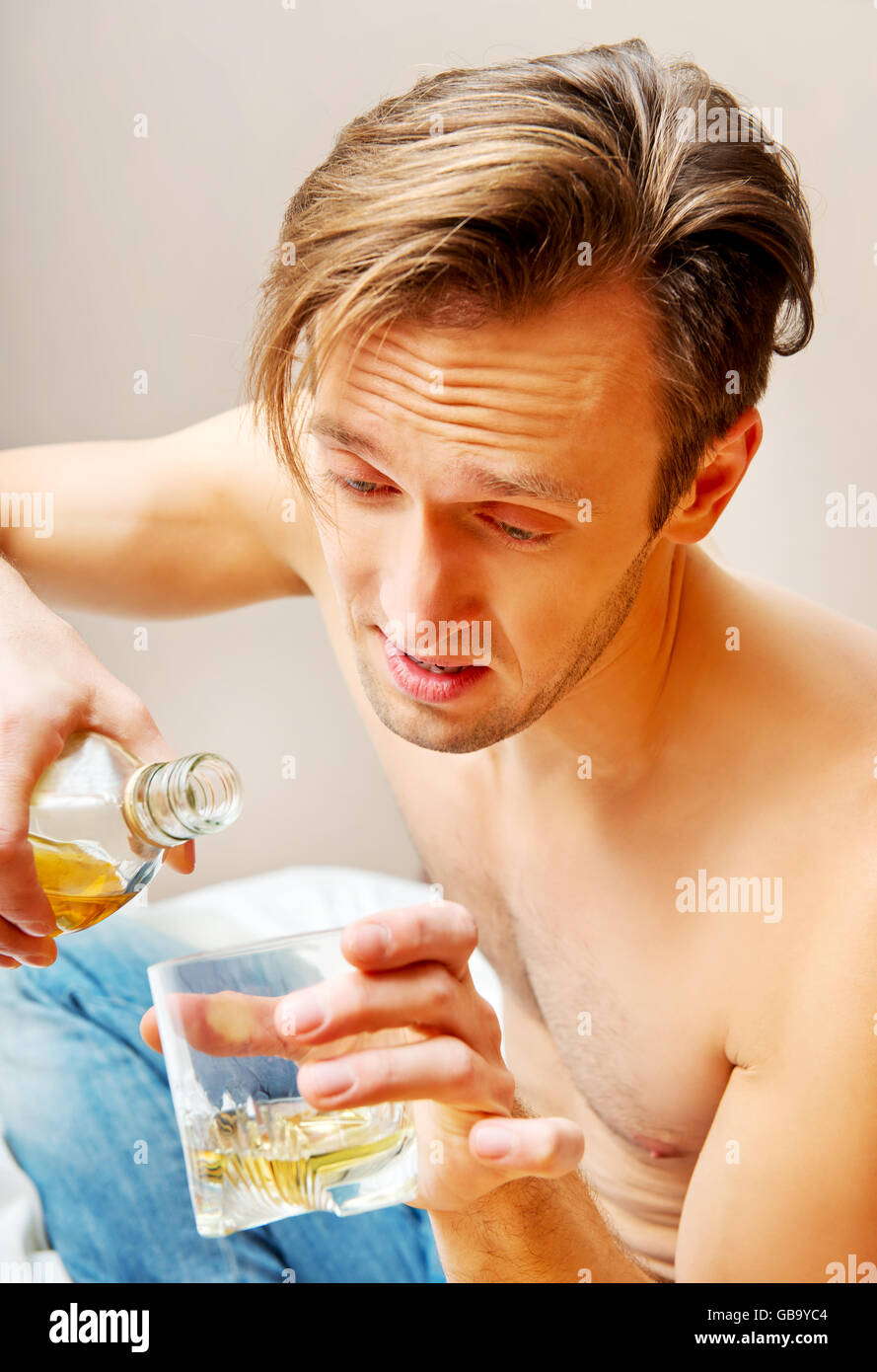 Drunk man sitting on bed and drinking whiskey Stock Photo