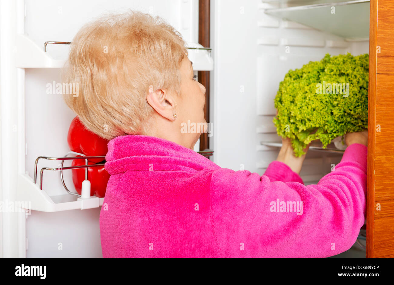 Senior woman taking a green lettuce from fridge Stock Photo