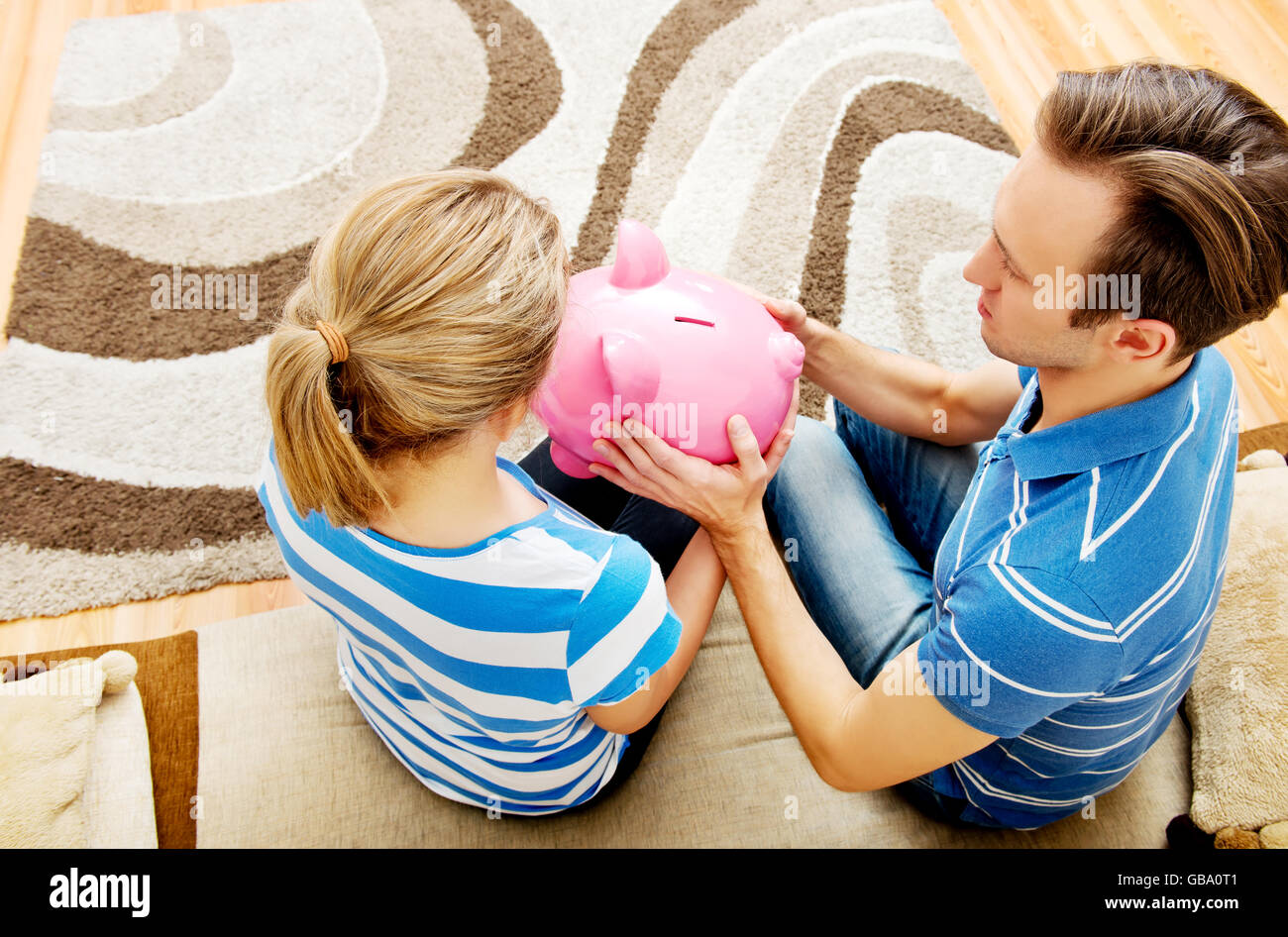 Back view of couple sitting on sofa with piggy bank Stock Photo - Alamy