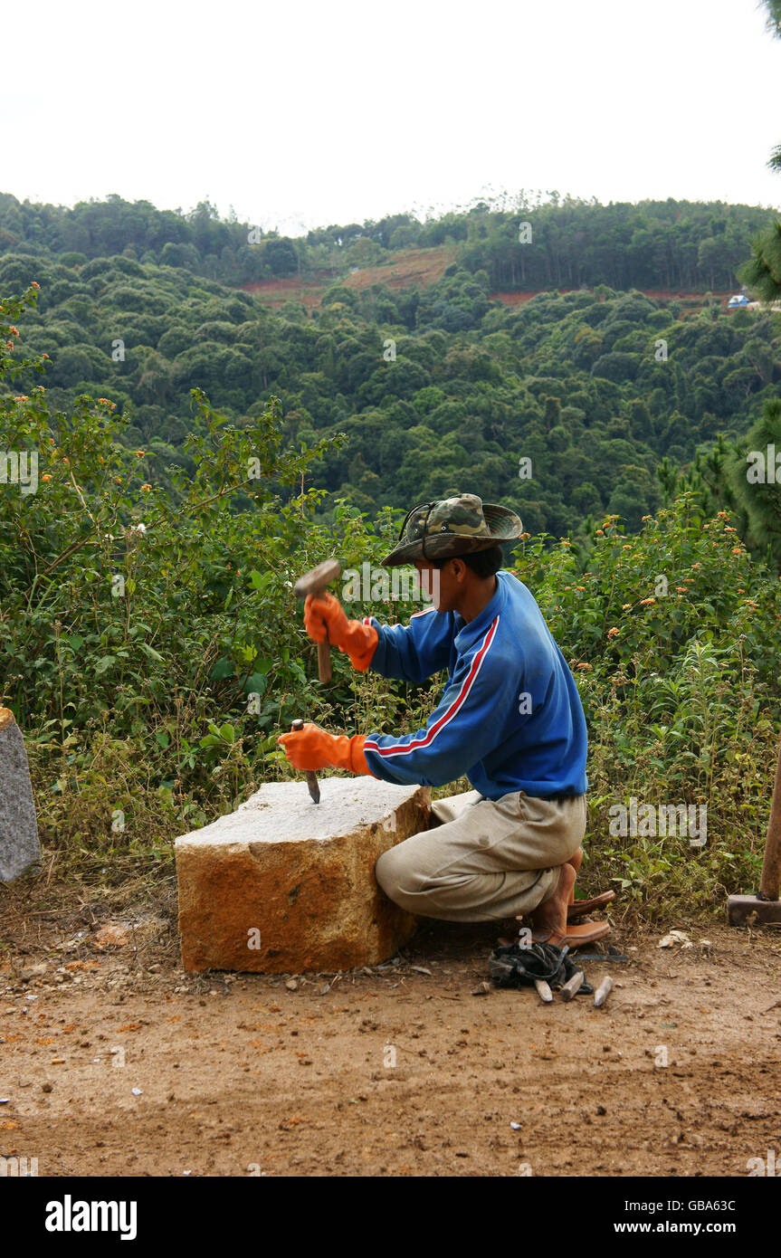 Two Workers with splitter on hand try to split large rock into small size for roadworks at