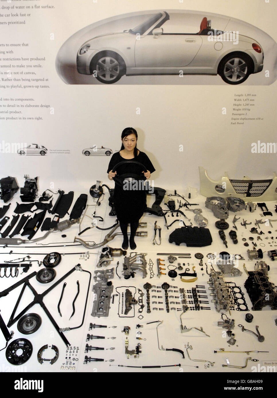 A woman stands among car parts of a Daihatsu Copen in the Science Museum in London. It is part of a new exhibition called 'Japan Car' which aims to showcase the future of car transport. Stock Photo