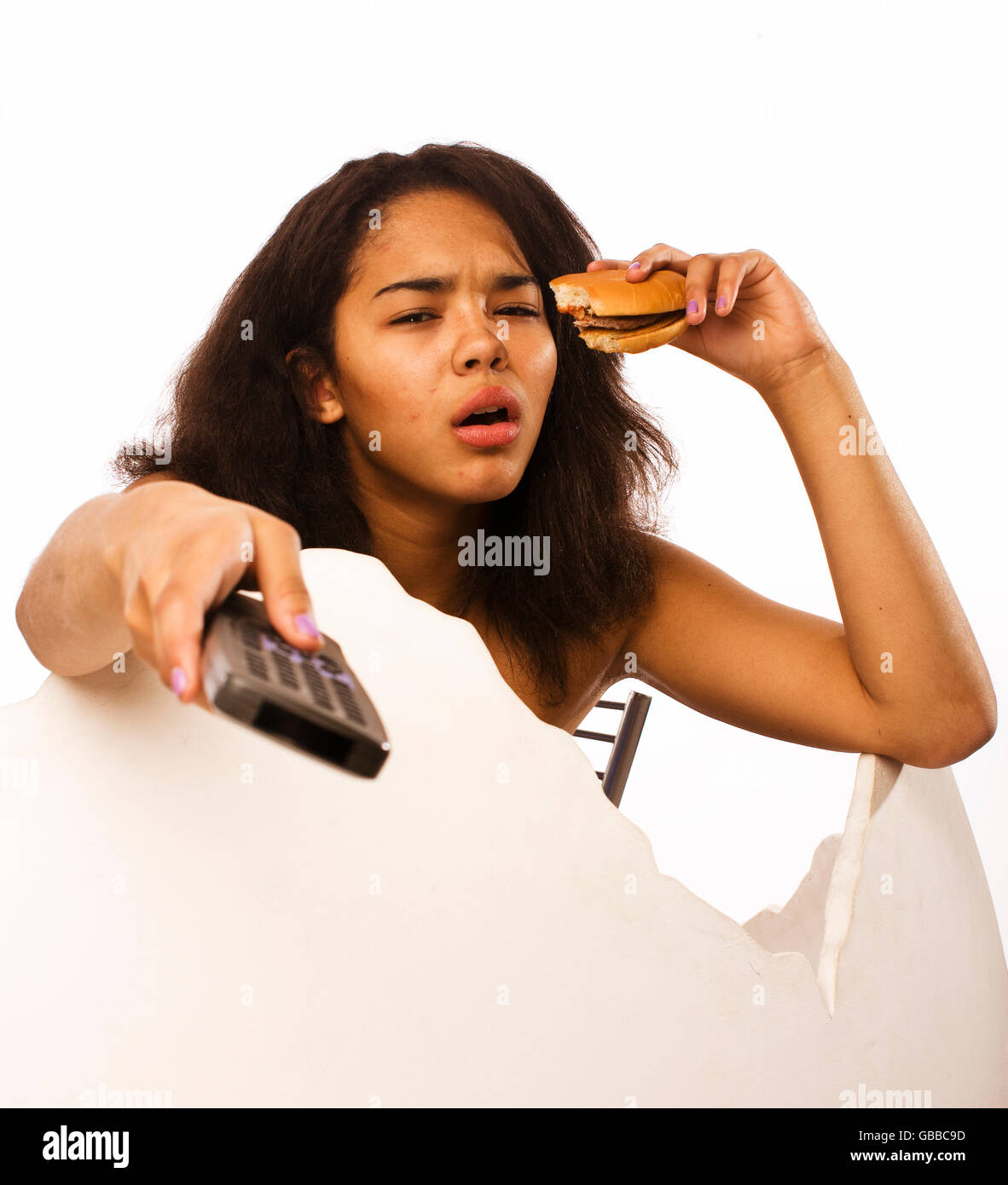 young fat african american teen girl with remote and hamburger isolated, unhealthy obsessed Stock Photo