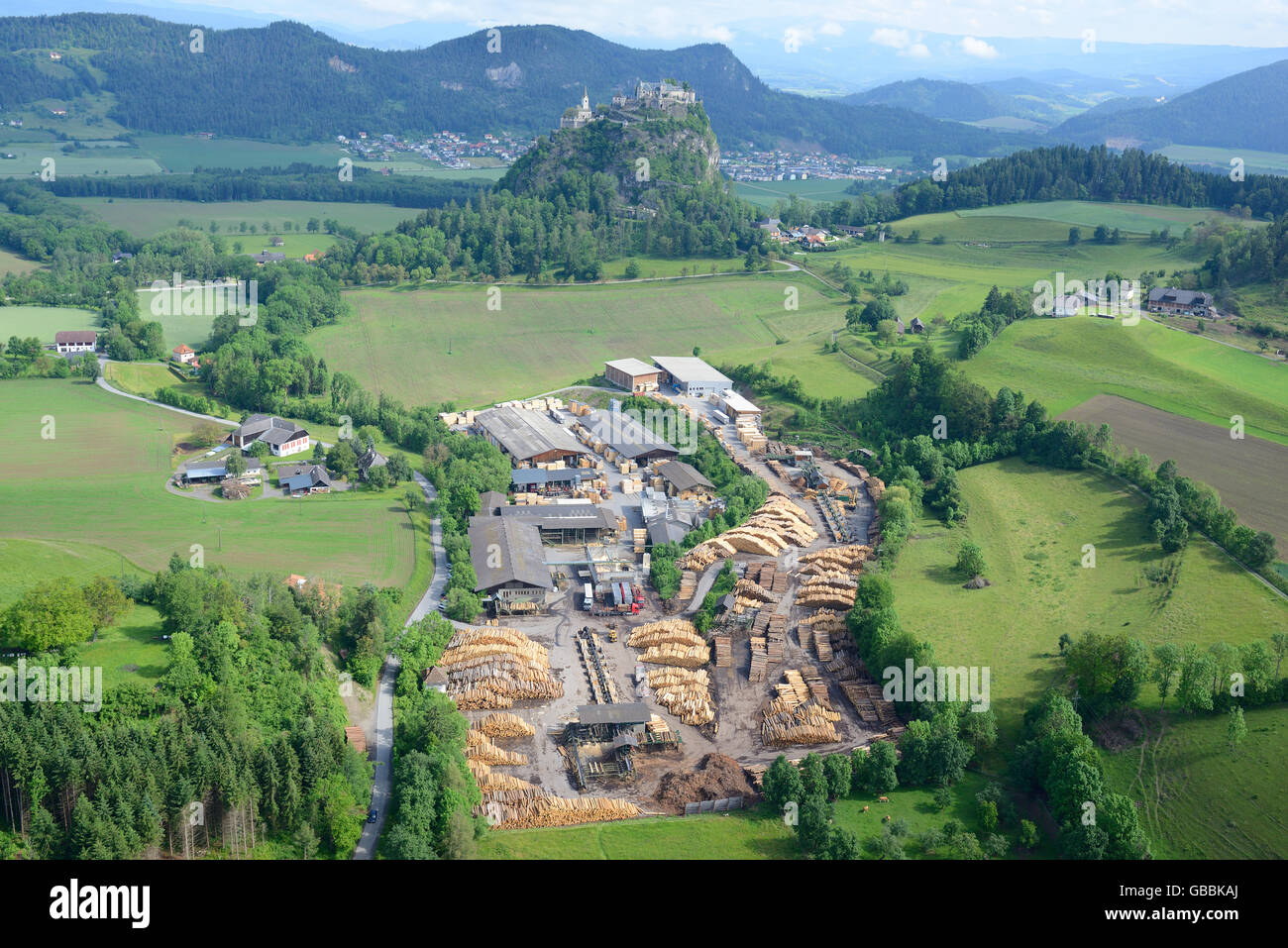 AERIAL VIEW. Sawmill with the perched medieval castle of Hochosterwitz in the distance. Hochosterwitz, Carinthia, Austria. Stock Photo