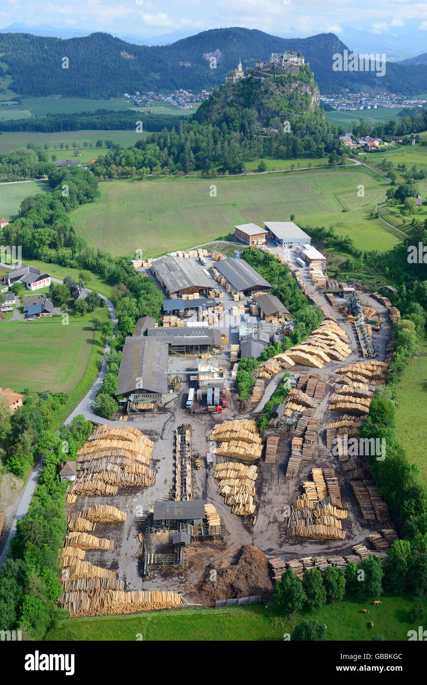 AERIAL VIEW. Sawmill with the perched medieval castle of Hochosterwitz in the distance. Hochosterwitz, Carinthia, Austria. Stock Photo