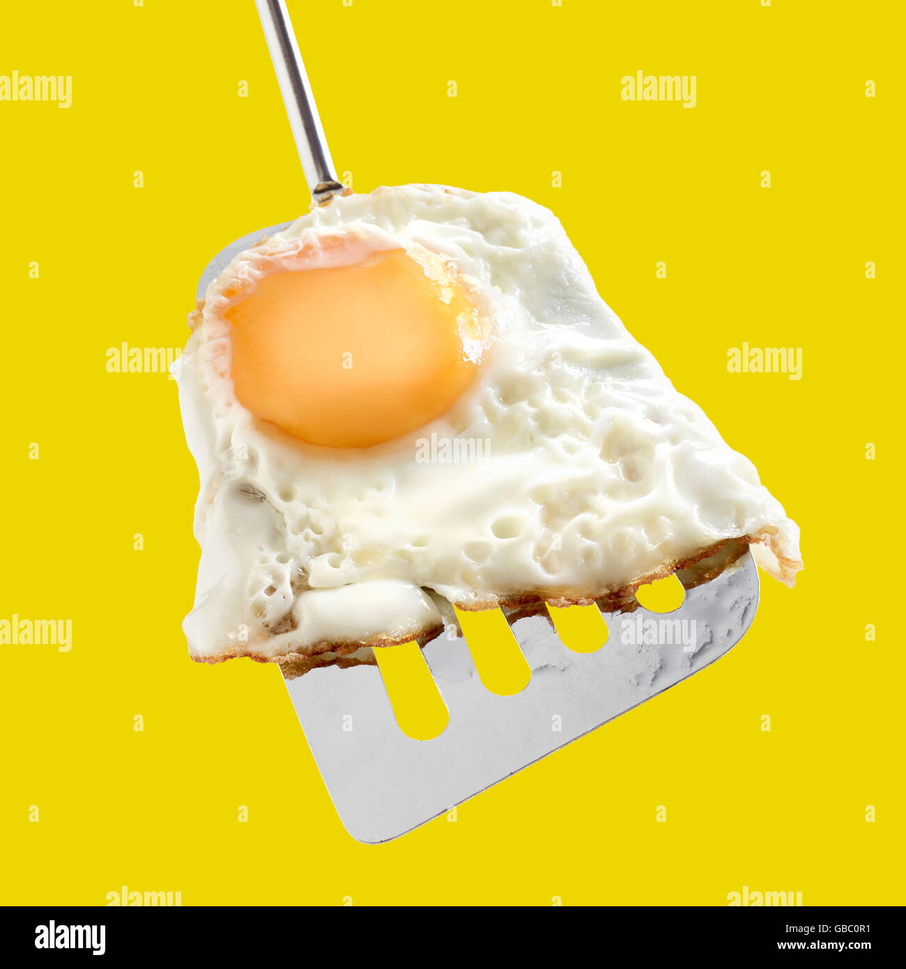 Fried egg, whole egg yolk on metallic spatula, yellow background Stock Photo