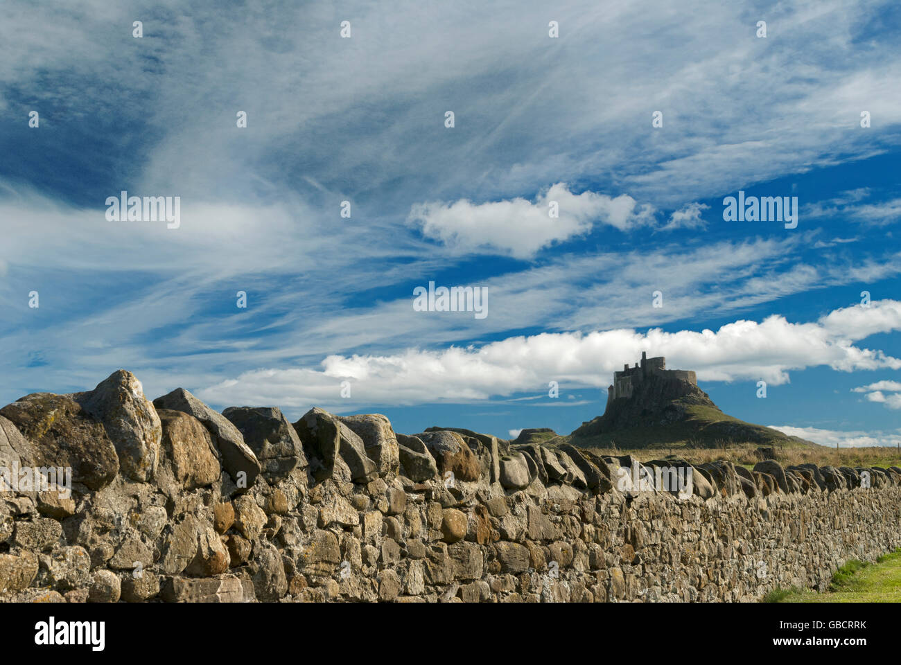 Lindisfarne Castle on Holy Island, Northumberland, under blue sky with light cloud, with a dry-stone wall Stock Photo