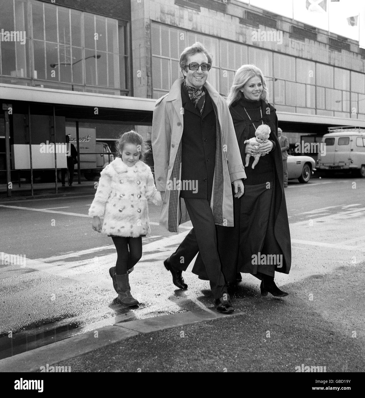 Actor Peter Sellers takes the hand of his daughter Victoria at Heathrow Airport, carrying her doll is her mother Britt Ekland, Sellers former wife. Stock Photo