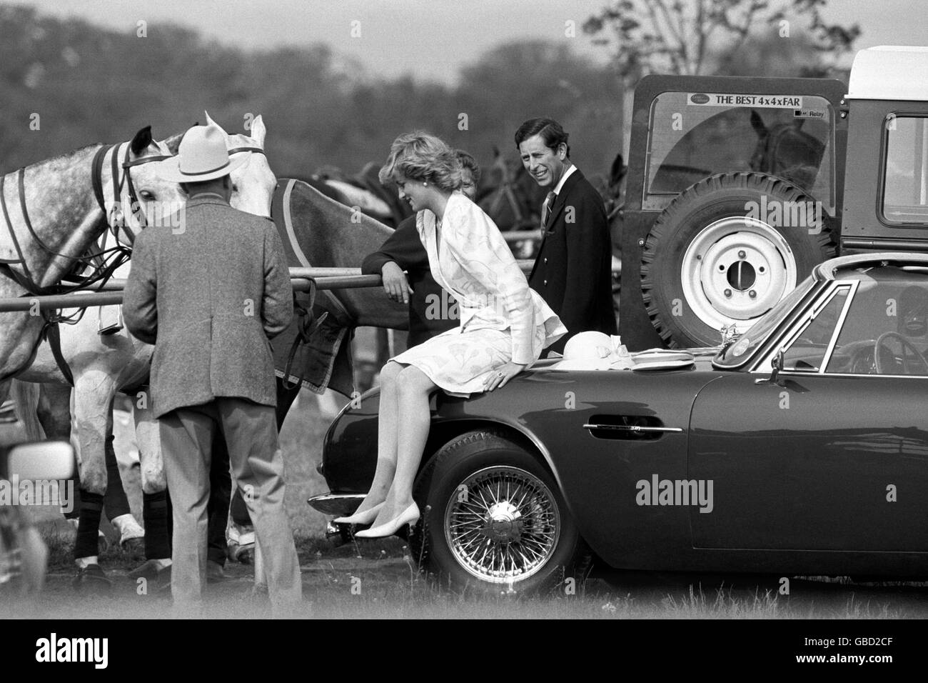 The Princess of Wales takes off her Ascot hat and takes a rest on the bonnet of her husband's Aston Martin car at a polo match at Smith's Lawn, Windsor. The Prince shares a joke as she does so. Stock Photo