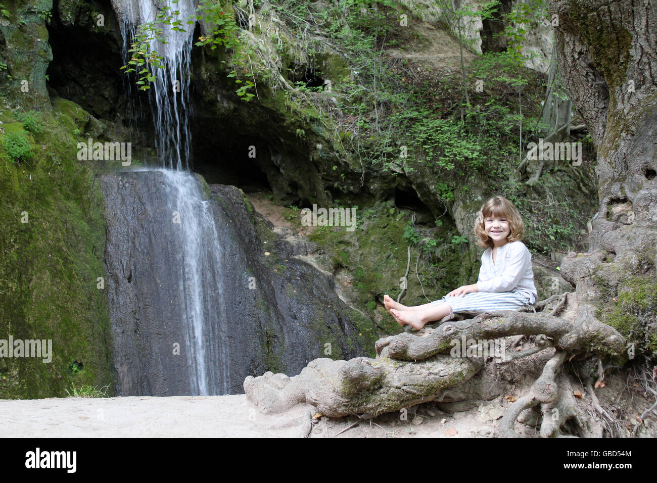 little girl sitting next to a waterfall Stock Photo