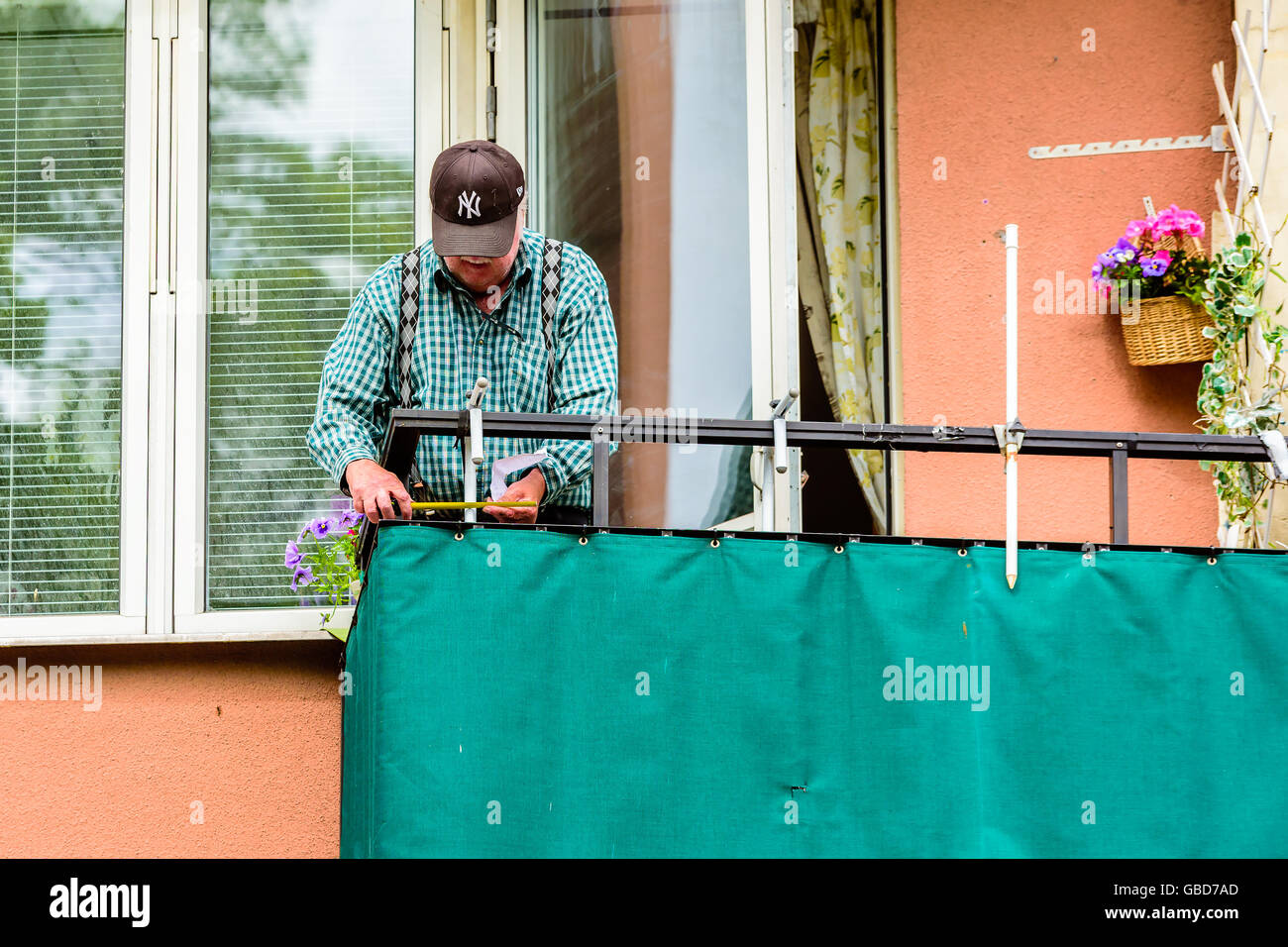 Motala, Sweden -June 21, 2016: Senior man measuring at a balcony. Ha has a small piece of paper in his hand as well. Stock Photo